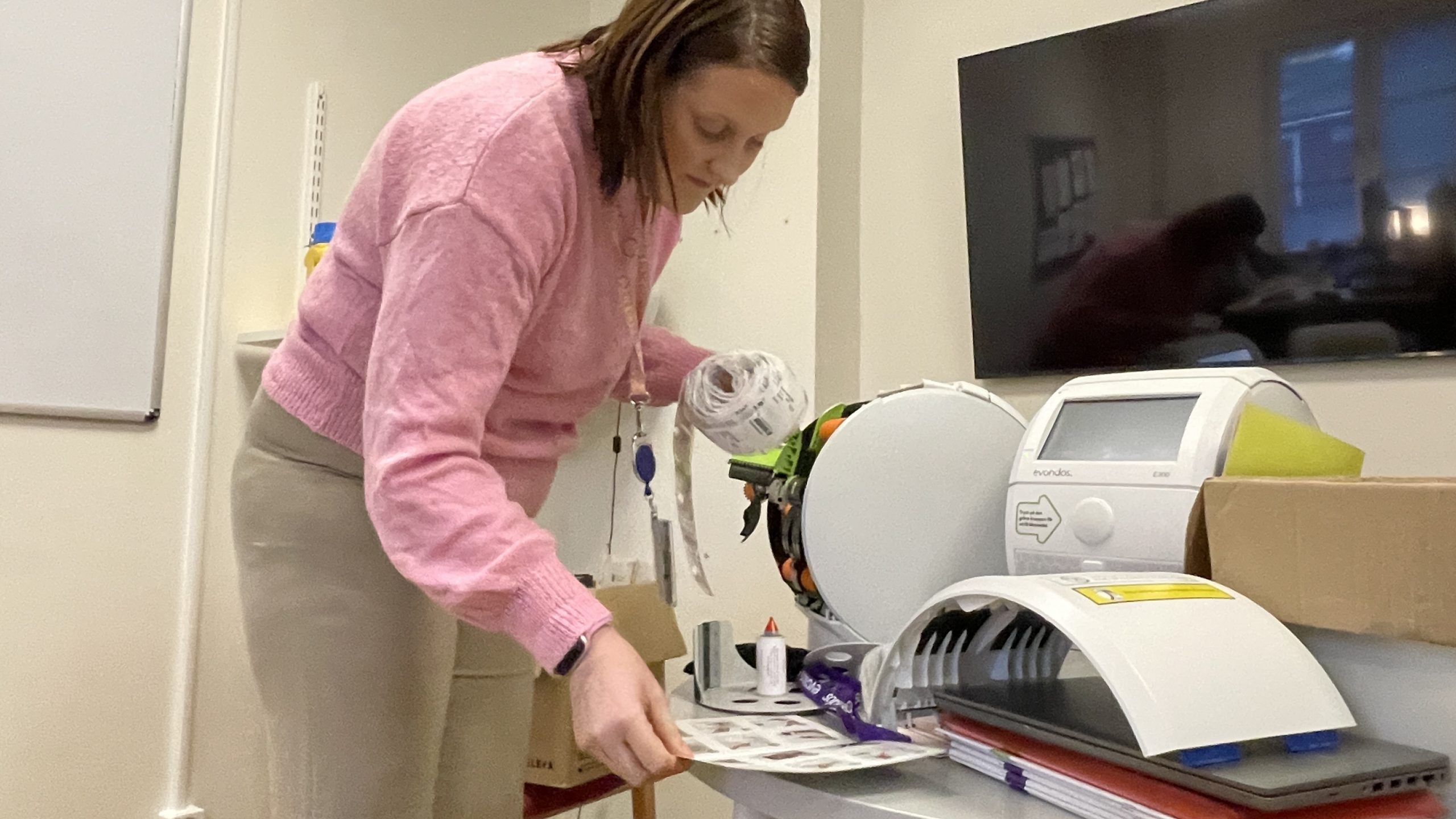 En kvinna i rosa tröja läser en instruktionsmanual och håller i en rulle med inplastade tabletter