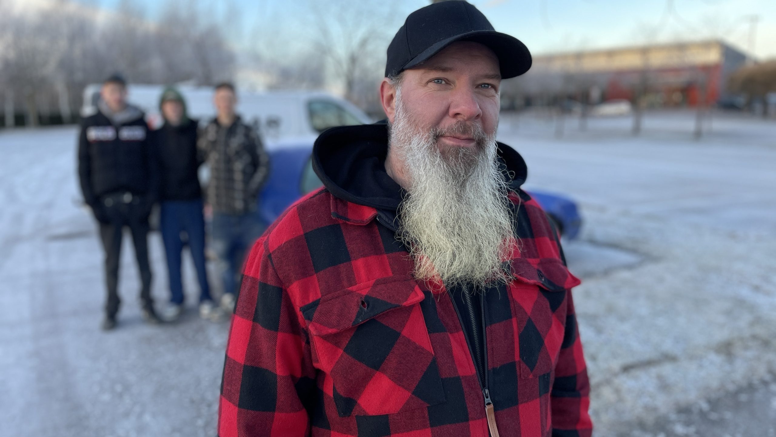 Man i röd rutig jacka framför ungdomar och blå A-traktor.