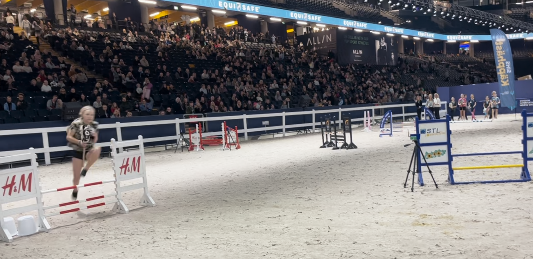 Käpphästryttare hoppar över hinder med hundratals åskådare på läktarna.