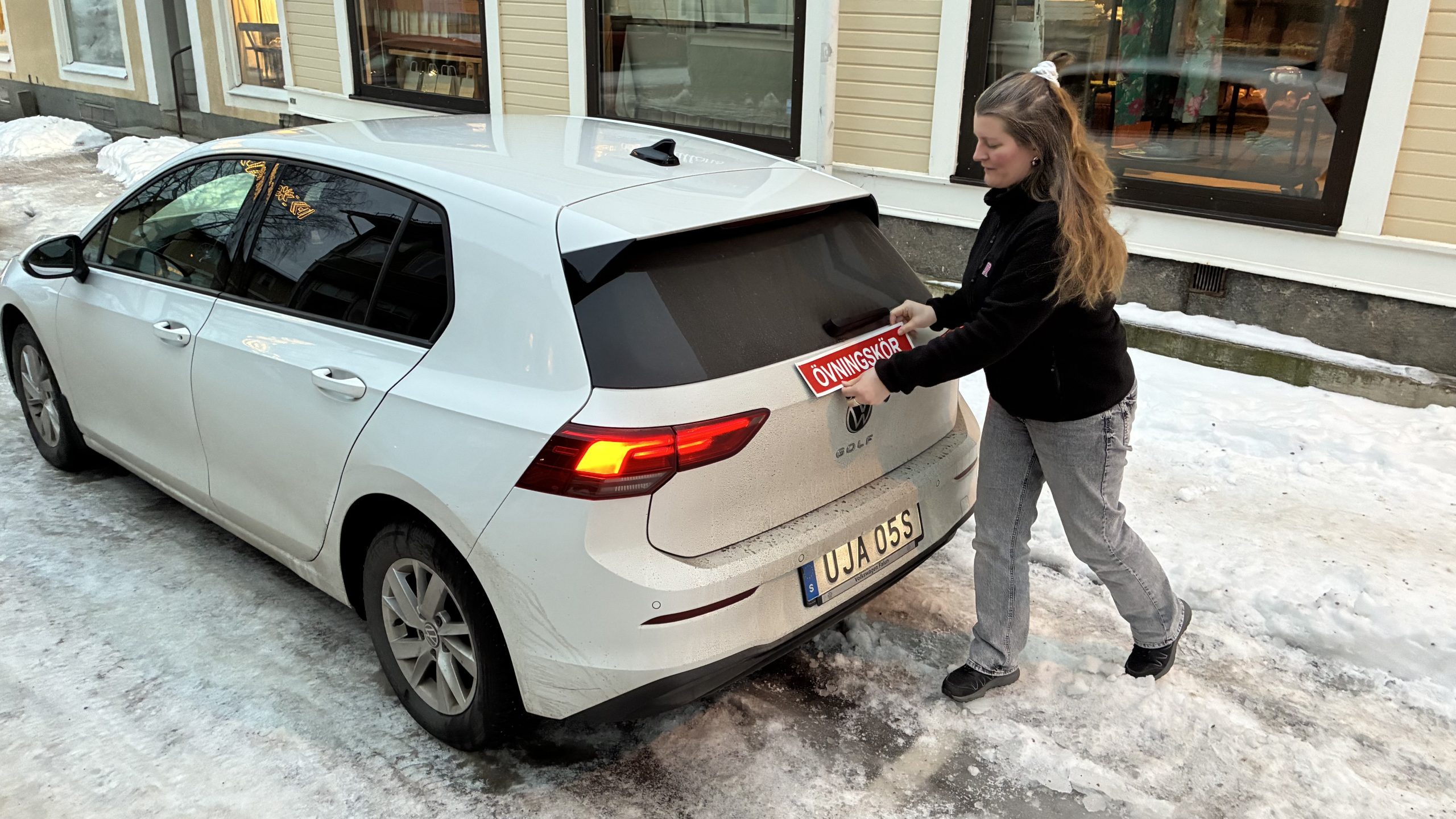 Alexandra Larsson sätter en röd övningskörningsskylt bak på en av trafikskolans bilar.