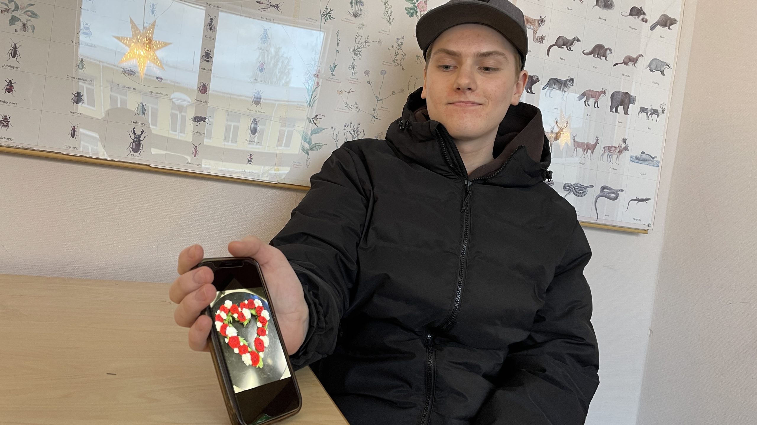Elev håller fram telefon med bild på hjärtformad blomuppsättning.