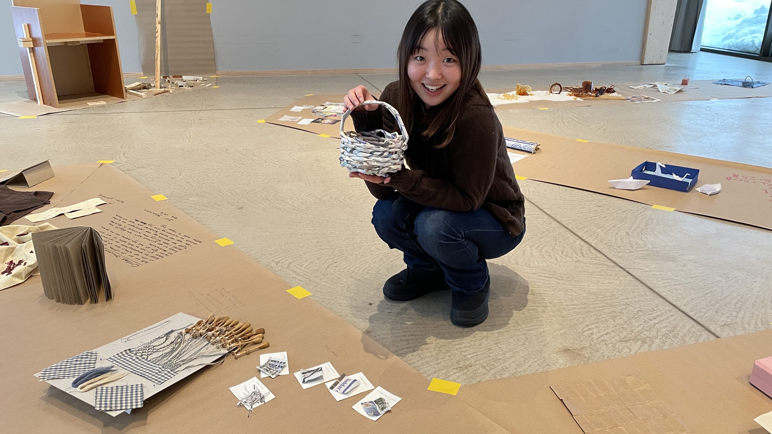 Elev håller upp en korg stor som en fotboll, flätad enbart av tidningspapper.