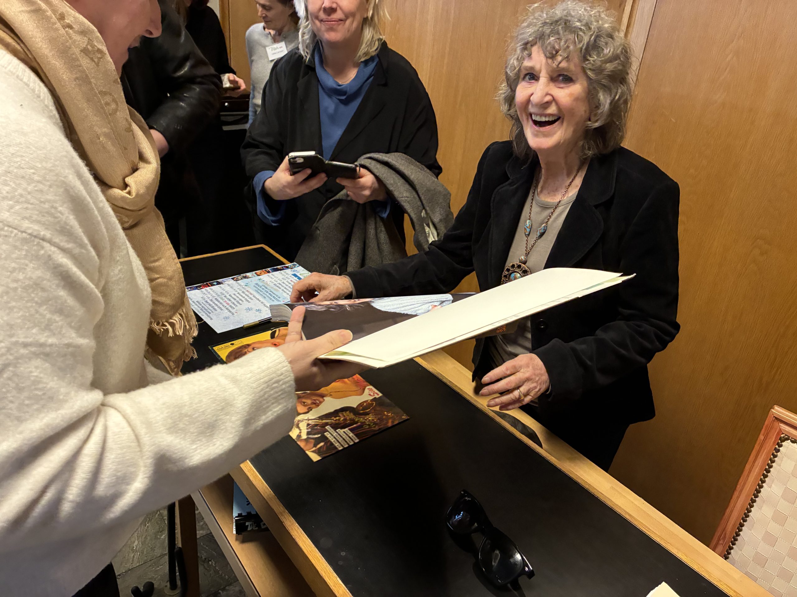 Siw Malmkvist ler brett mot kameran samtidigt som hon skriver autografer.