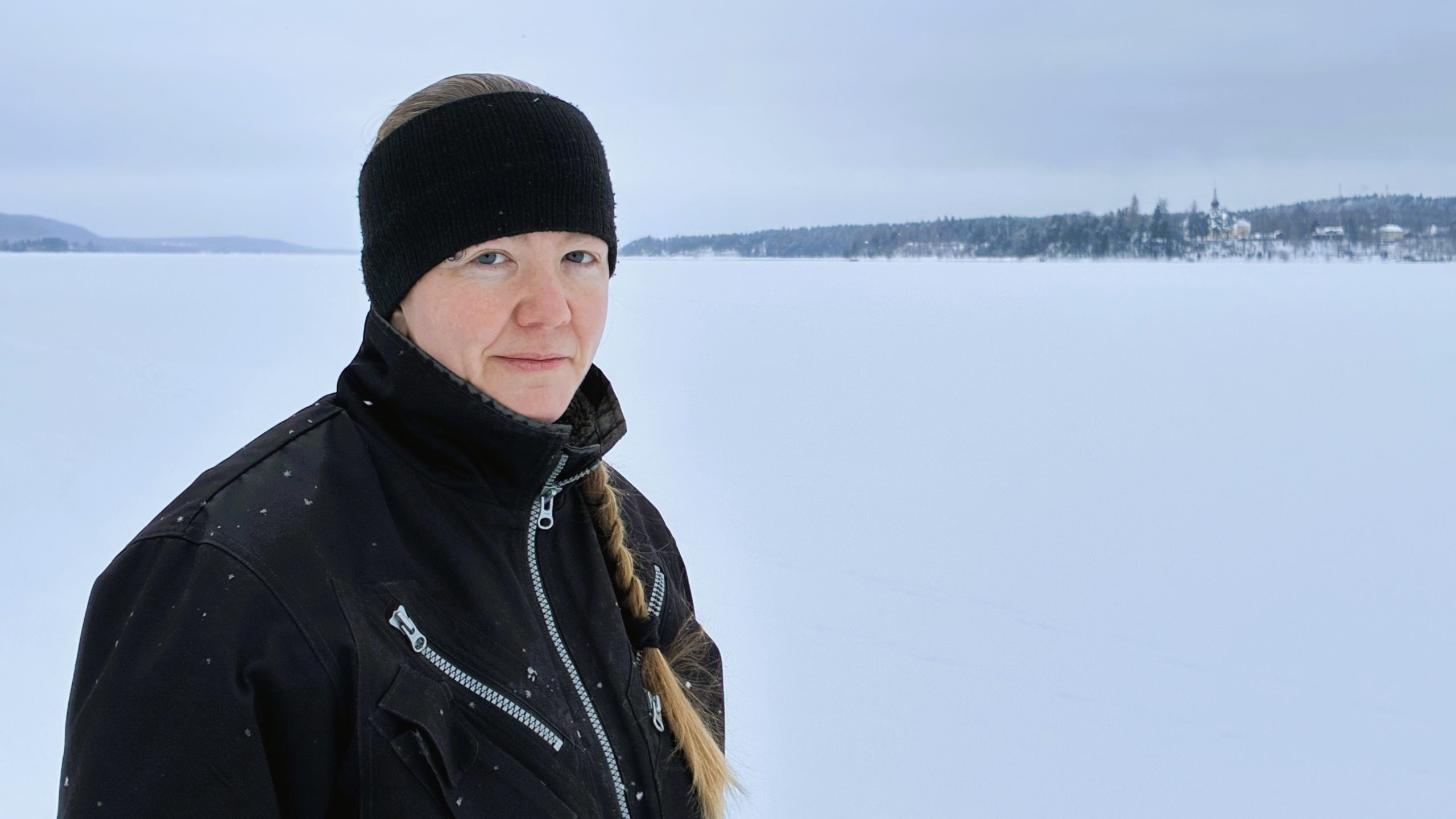 Kvinna står i vinterkläder framför den frusna sjön Siljan.
