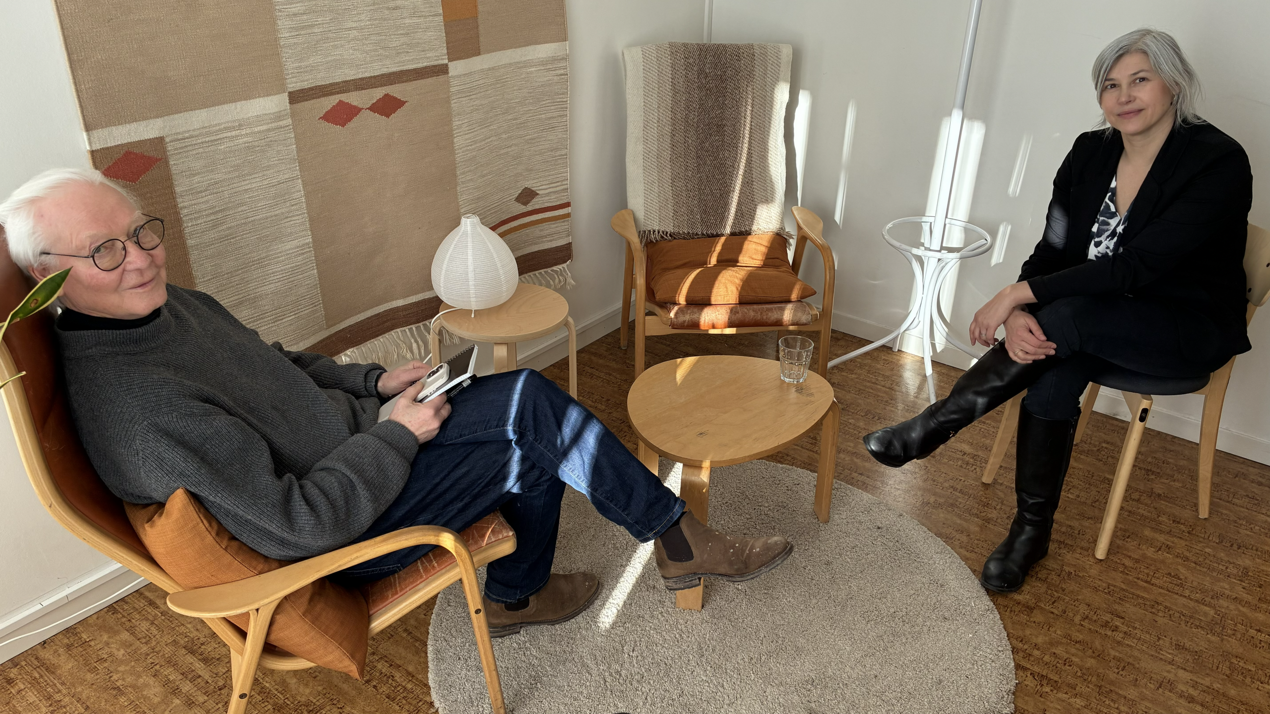 Två personer sitter i fåtöljer i ett mötesrum.