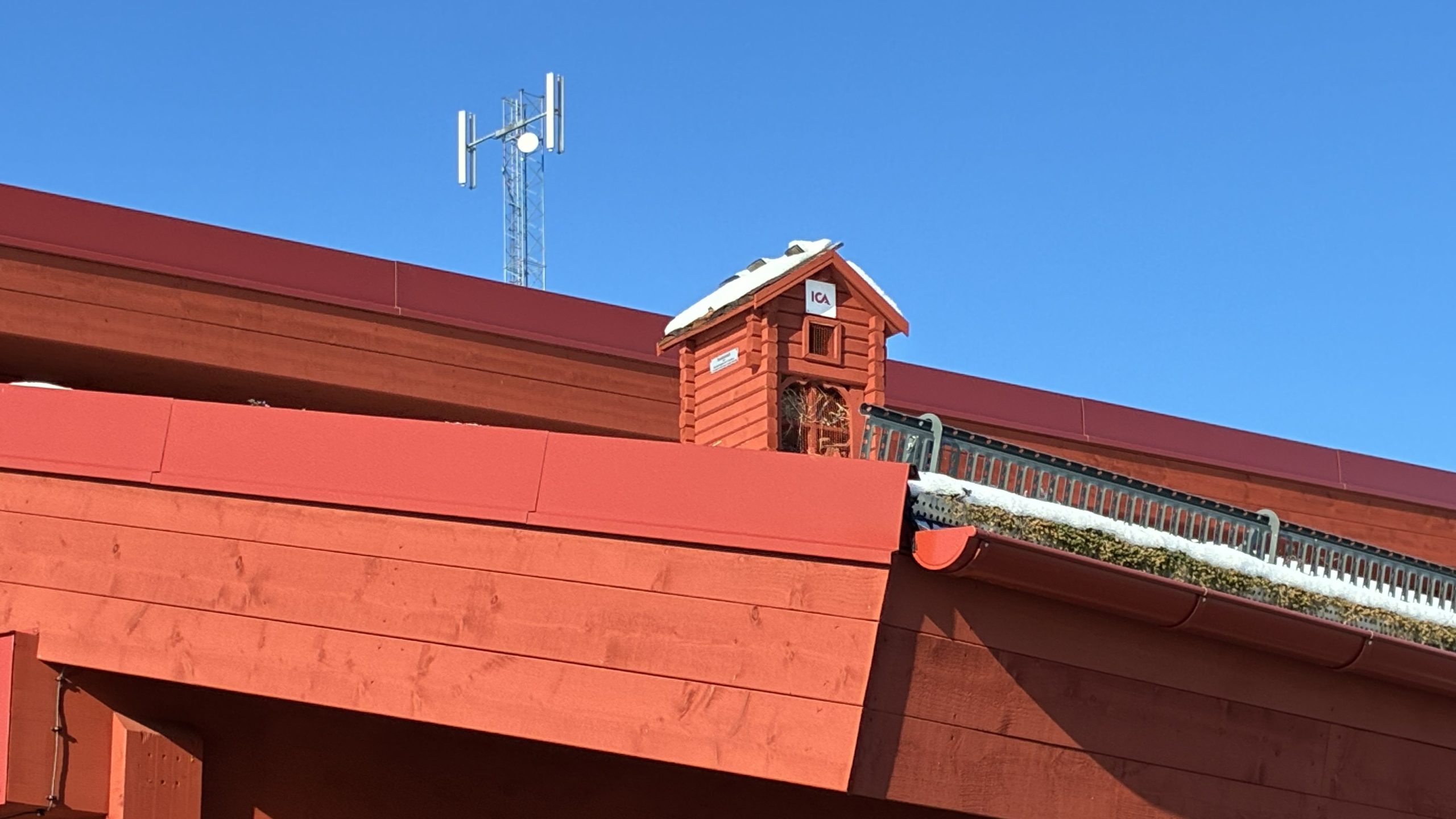 Inzoomad bild på det lilla insektshotellet, även det byggt i "timrat" trä med Falu rödfärg.