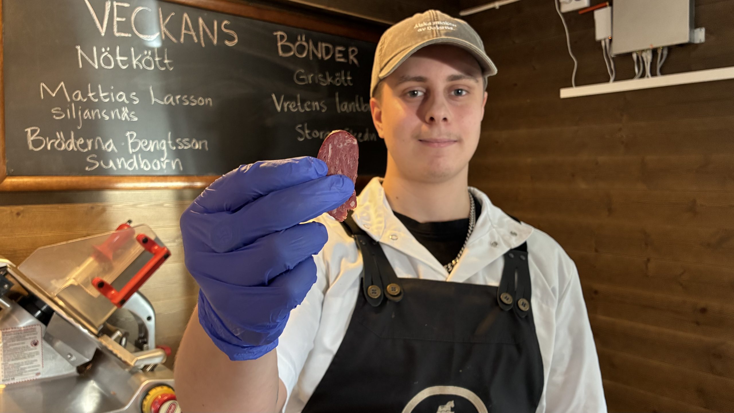 Ung man håller fram korvbit mot kameran.