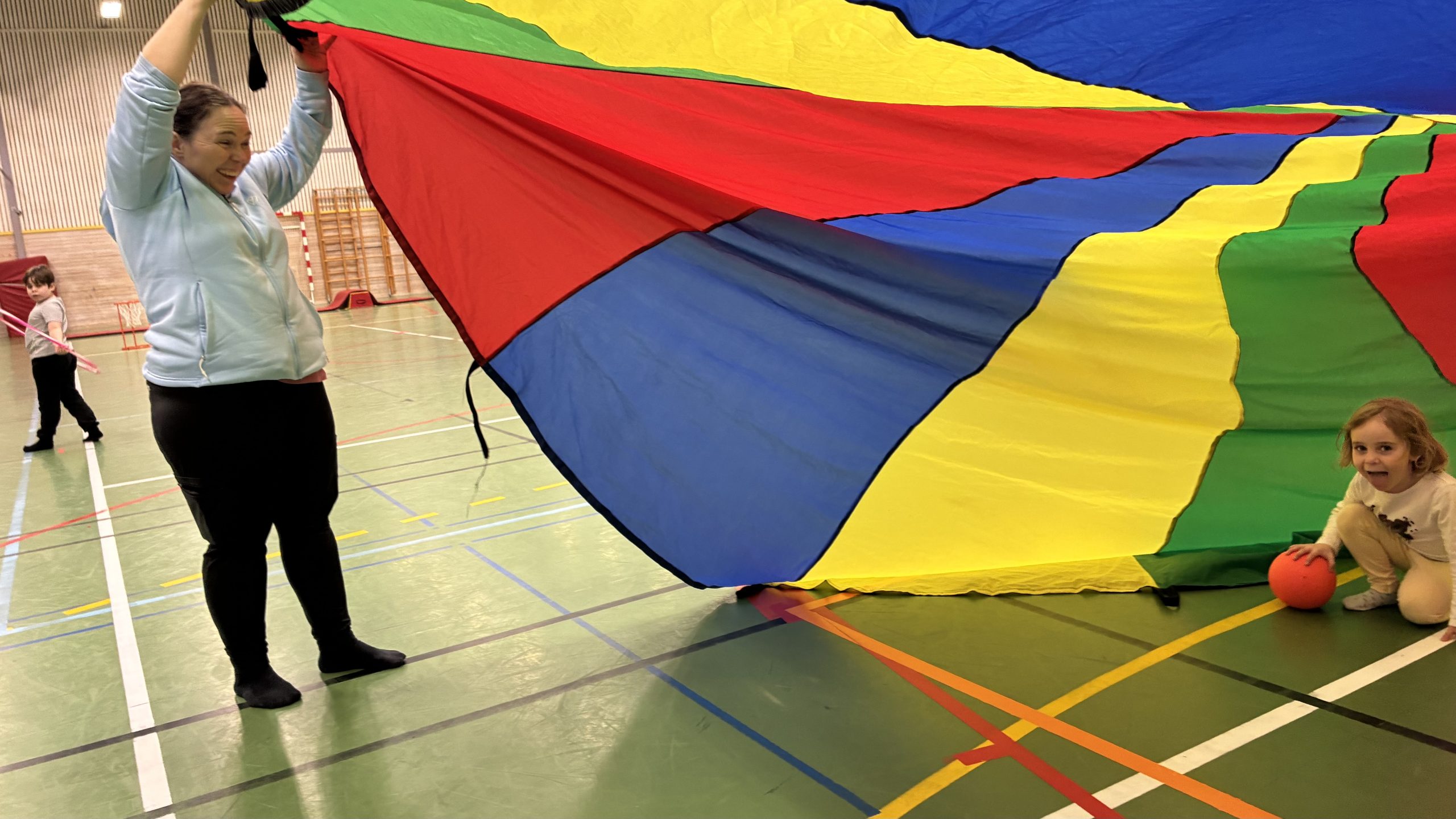 Treåring kryper genom ett mångfärgat tält och ler mot kameran med utsträckt tunga