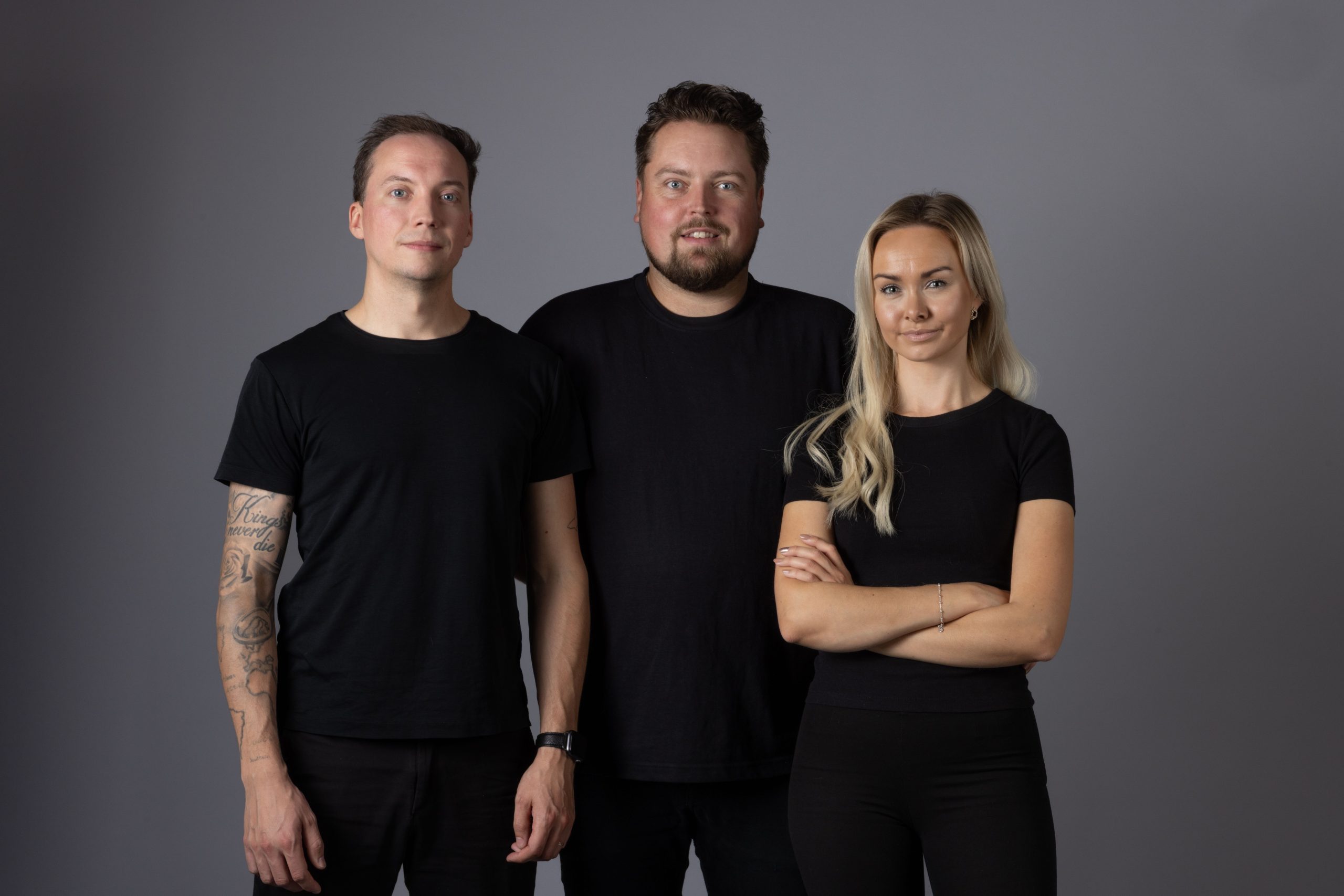 Tre personer i mörka kläder poserar framför kameran i en fotostudio.