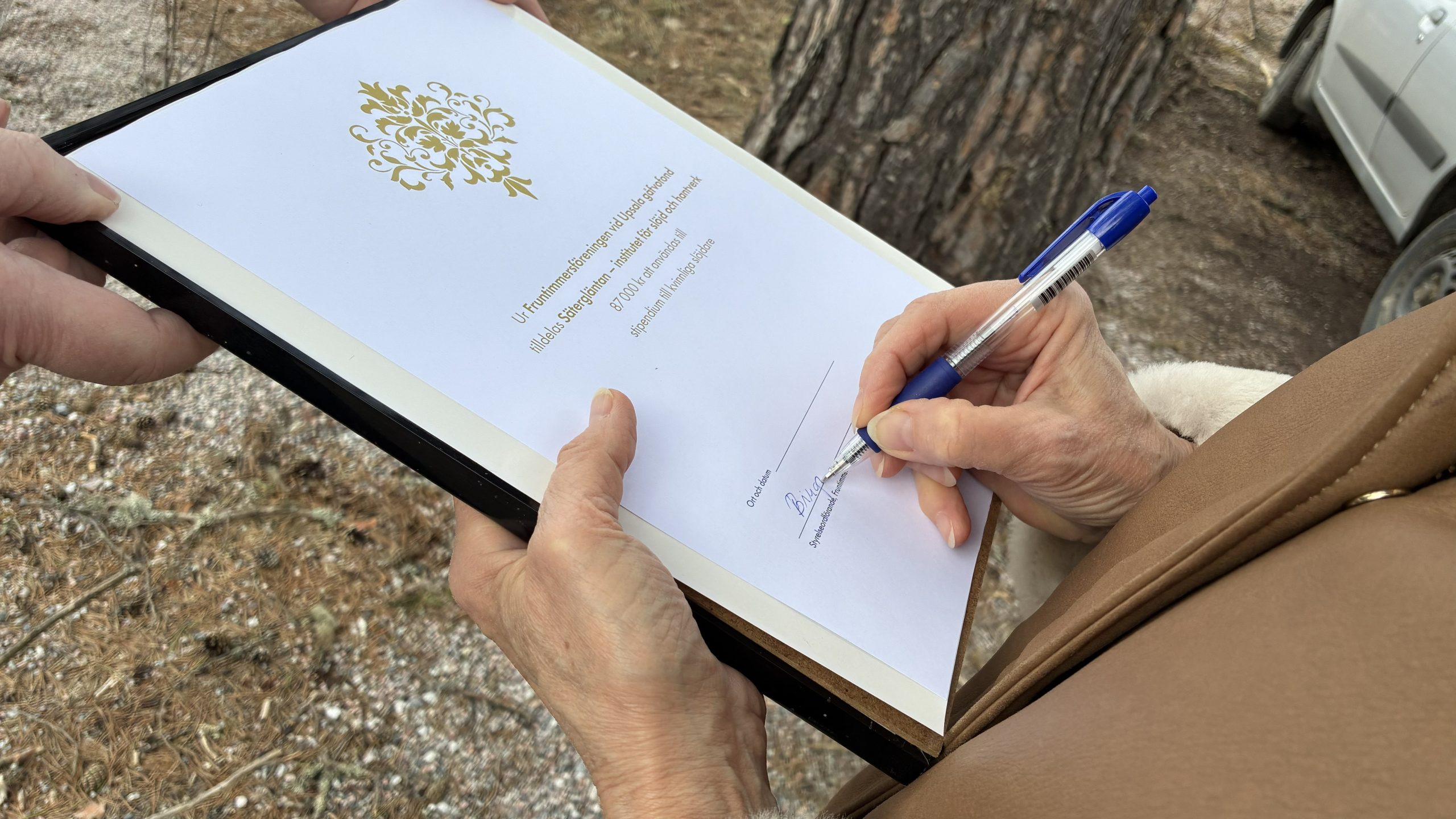 Hand med penna skriver under ett diplom som bekräftar utdelningen.