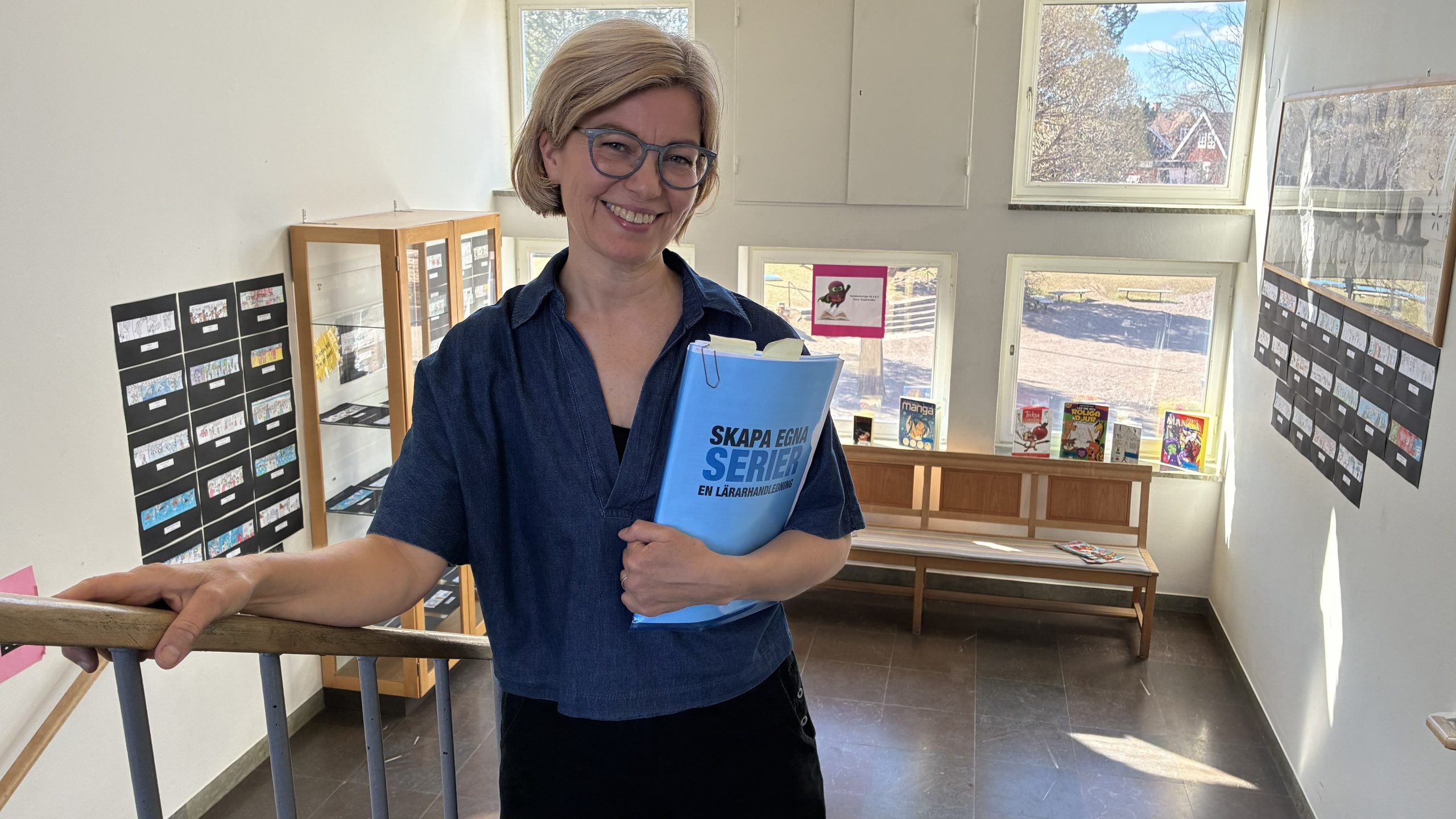 Anna Walsh fotograferad i en trappa, i famnen håller hon kompendiet "Skapa egna serier".