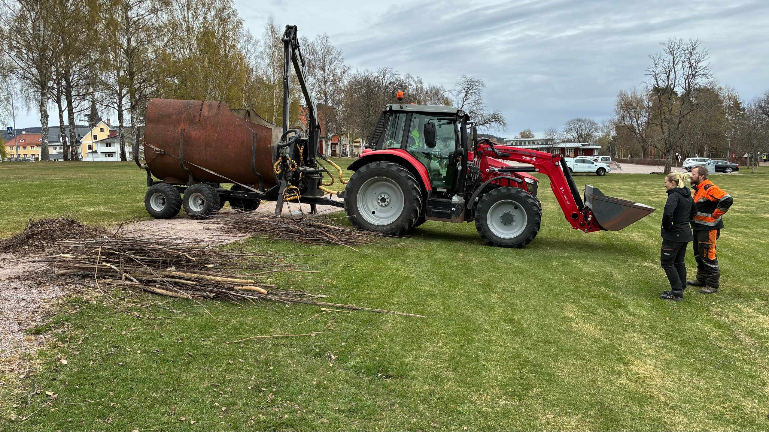 Traktor lyfter upp träpinnar och lägger dem på en vagn.
