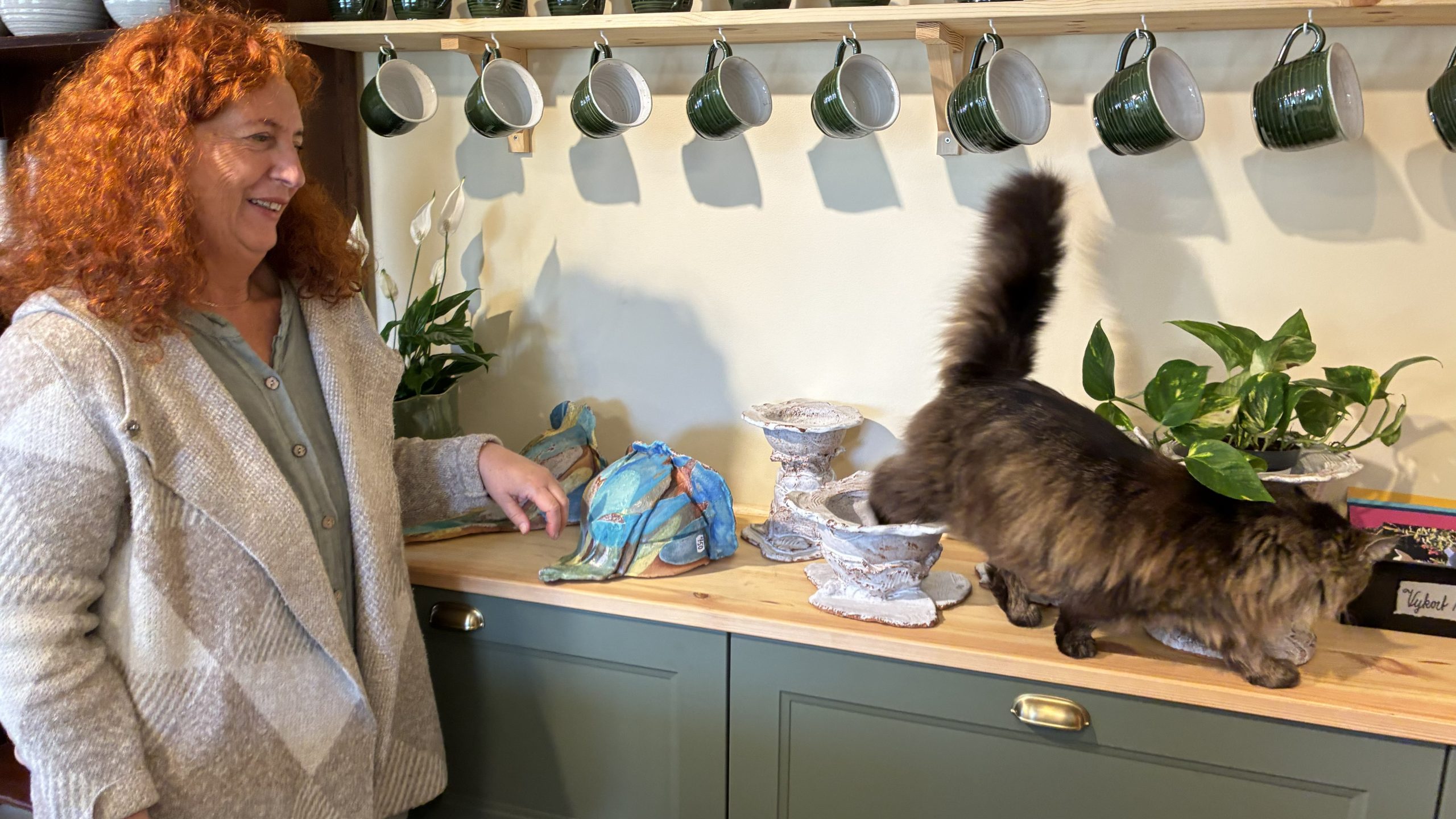 En katt vandrar på en hylla med keramik, så nära att hon till och med sätter tassen i en av skålarna.