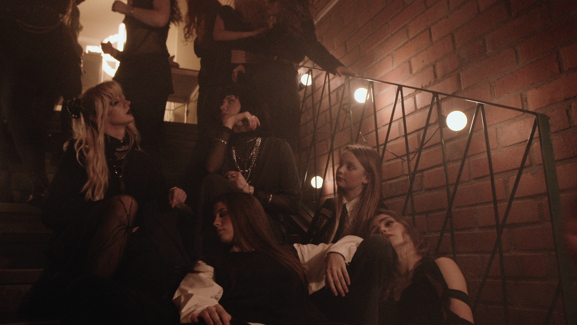 Kvinnor sitter tätt i en dunkelt upplyst trappa som mer liknar en nattklubbsbyggnad än en skola.