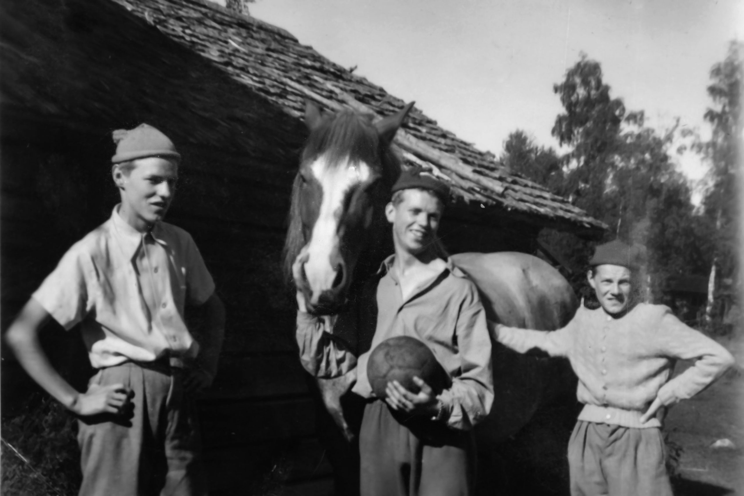 Tre pojkar i 20-årsåldern poserar med en häst på en svartvit bild.