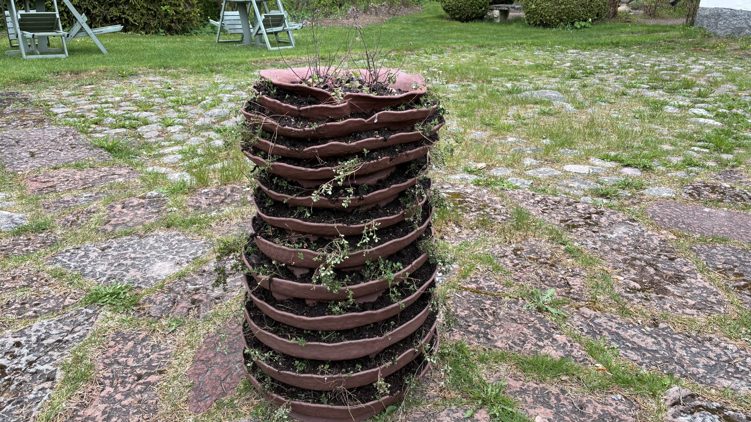 Skulptur i form av en kruka med flera lager av jordbäddar där det växer örter, kanske backtimjan.