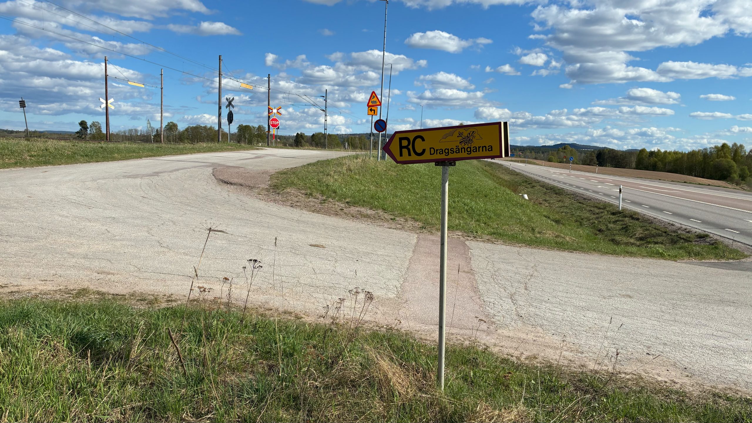Skylt som pekar mot RC Dragsängarna, i bakgrunden järnvägsövergången och en skylt som varnar för den.