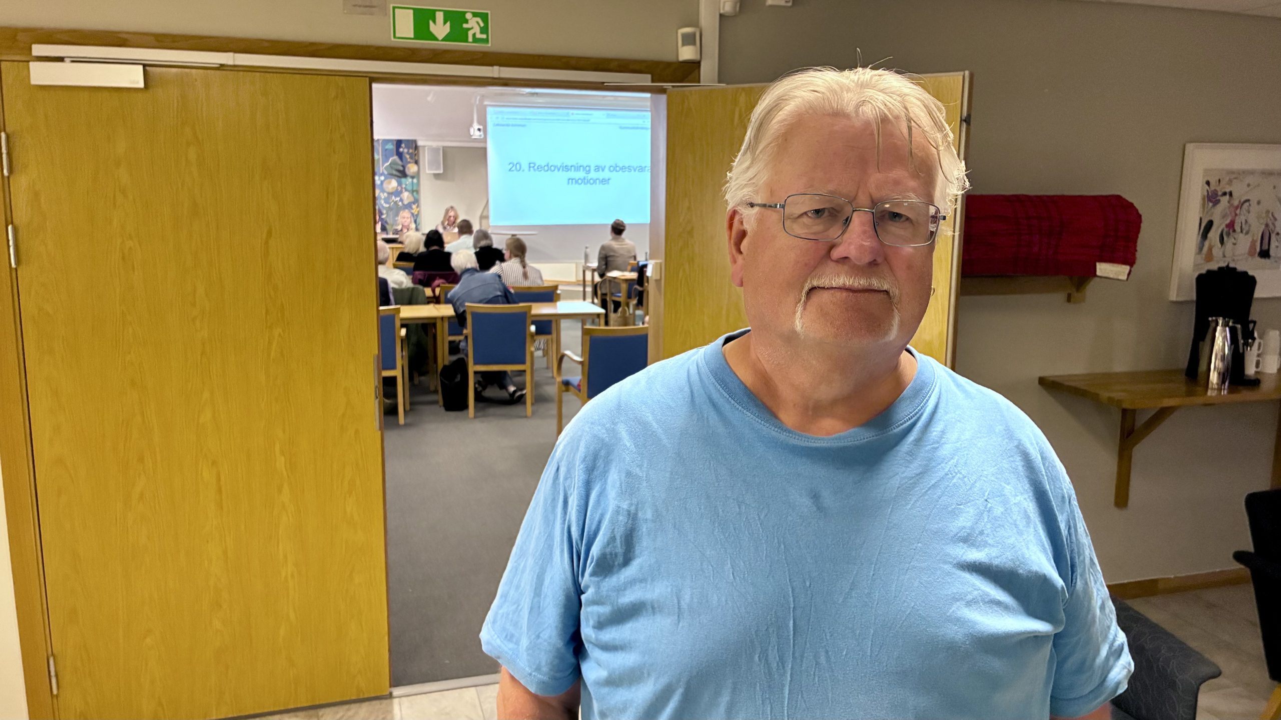 Man i blå tröja med besviket ansiktsuttryck i foajen utanför plenisalen.