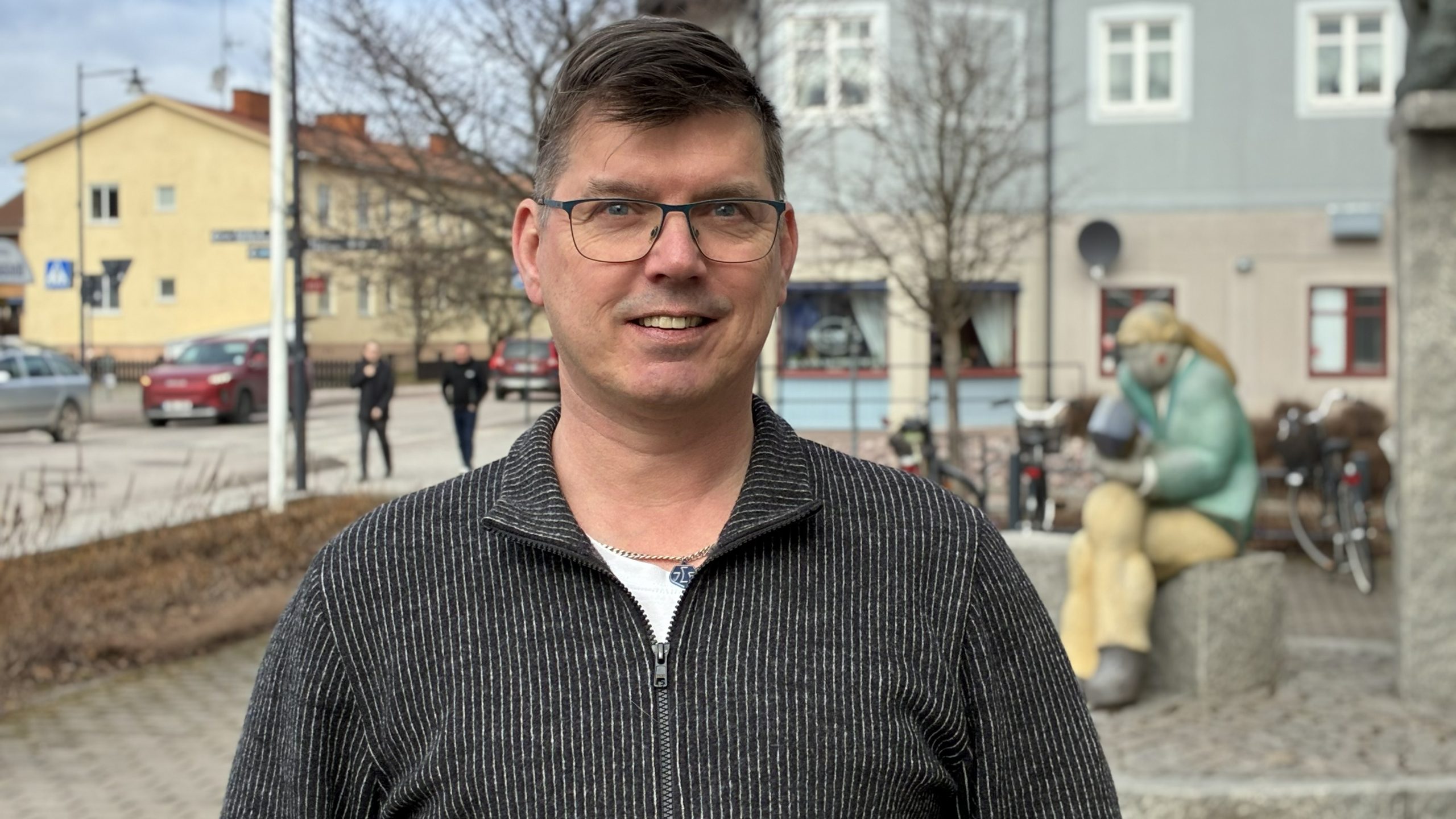 Johan Fändriks tittar in i kameran med en skulptur vid Leksands kommunhus i bakgrunden.