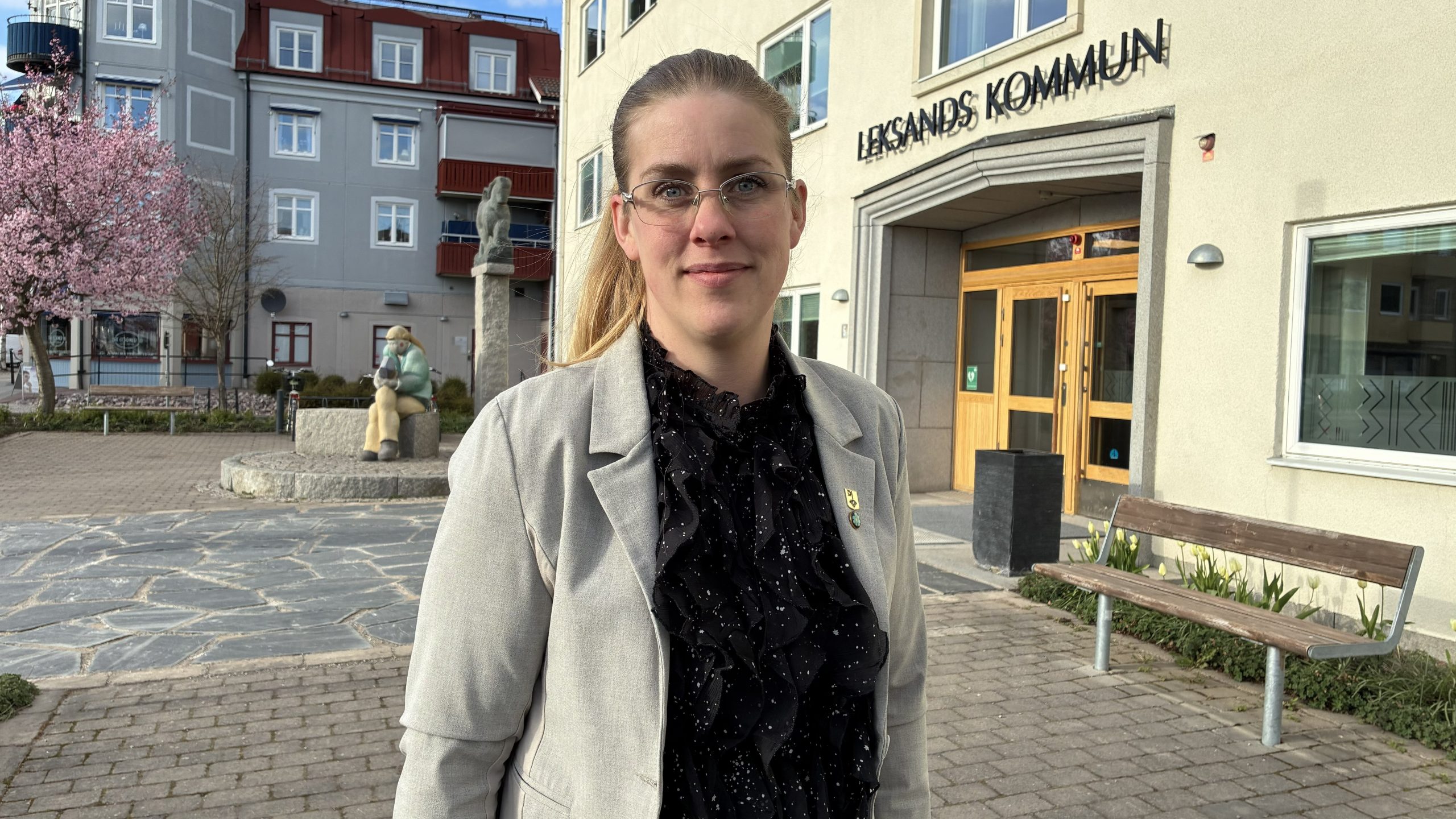 Lina Ruuth i kavaj med en pin med Leksands kommunsymbol. I bakgrunden syns entrén till Leksands kommunhus.