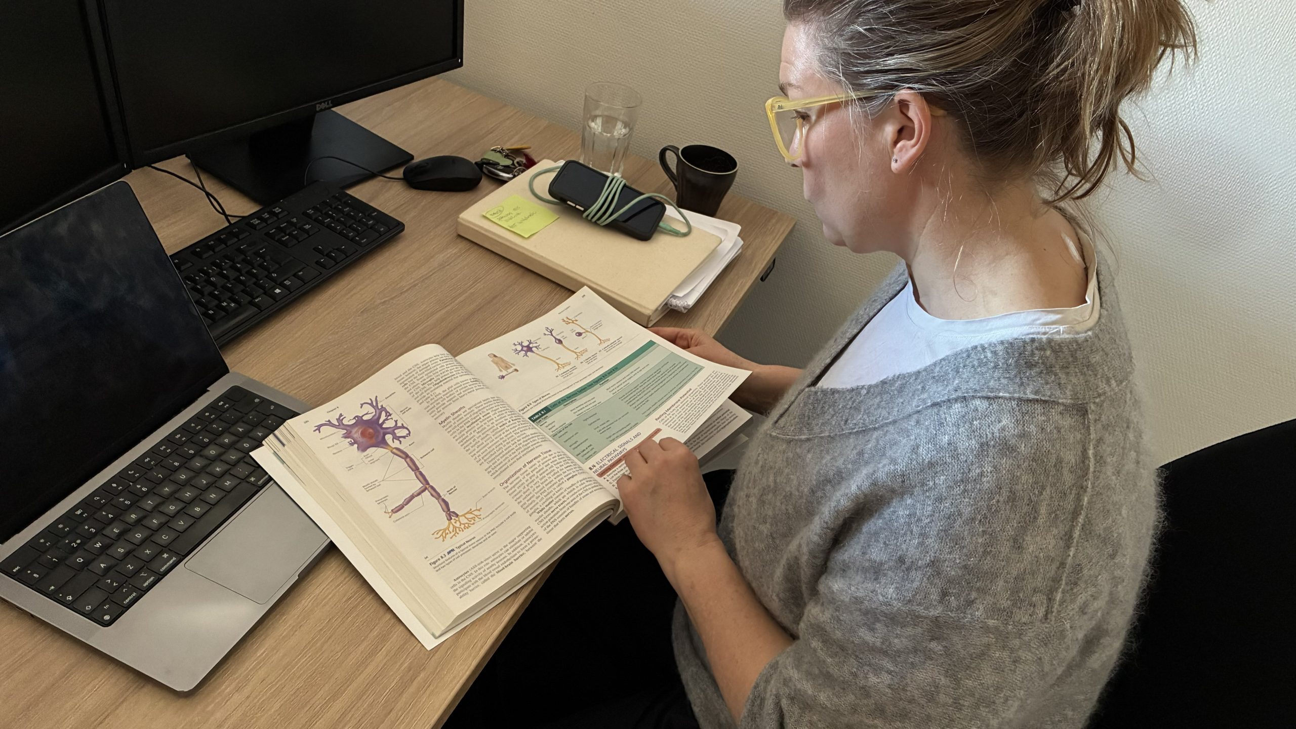 Louise bläddrar i en tjock lärobok med en bild på nervsystemet.