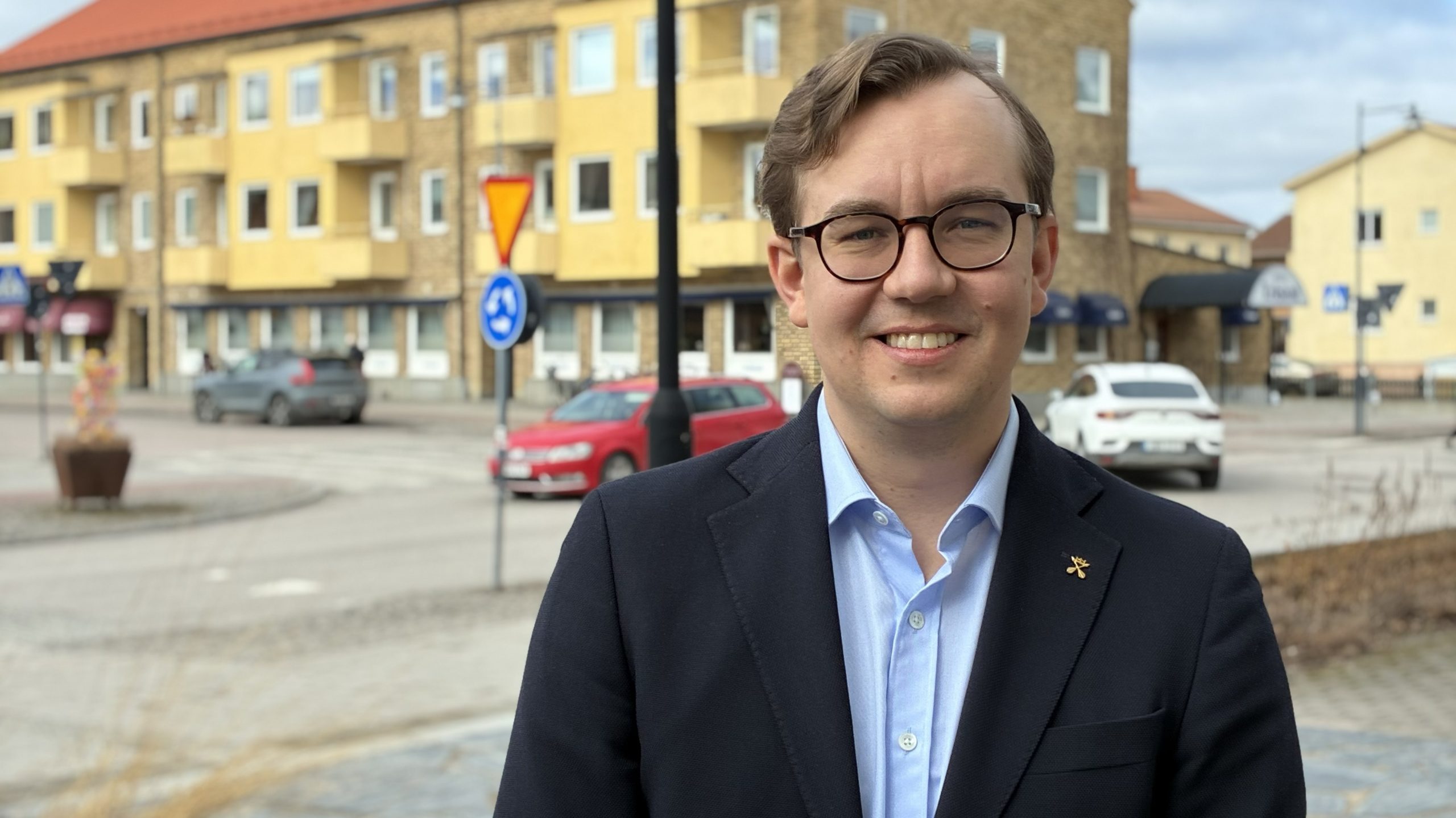 Man i kavaj och blå skjorta tittar in i kameran med utsikt mot centrala Leksand.