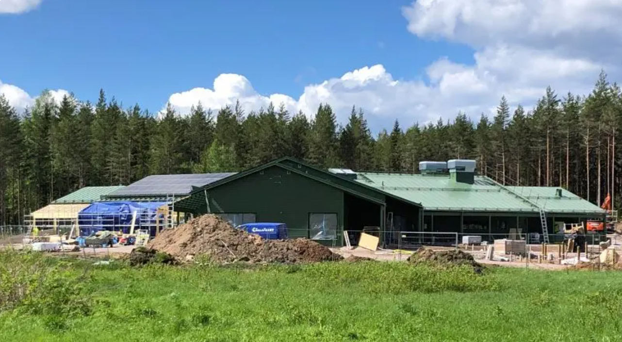 Halvfärdig byggnad med jordhögar och maskiner i förgrunden.