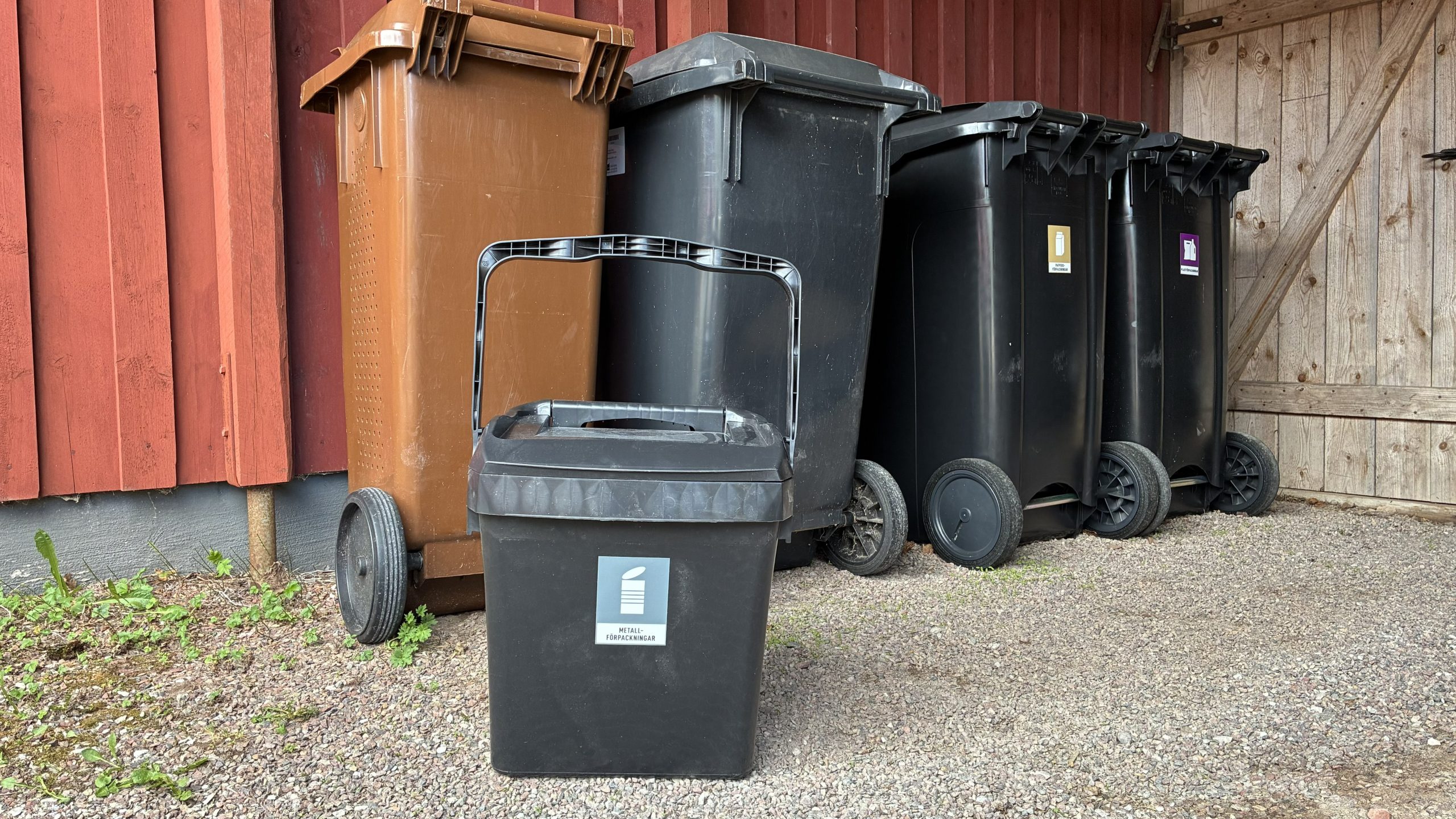 Metallåtervinningsboxen står framför fyra andra soptunnor.