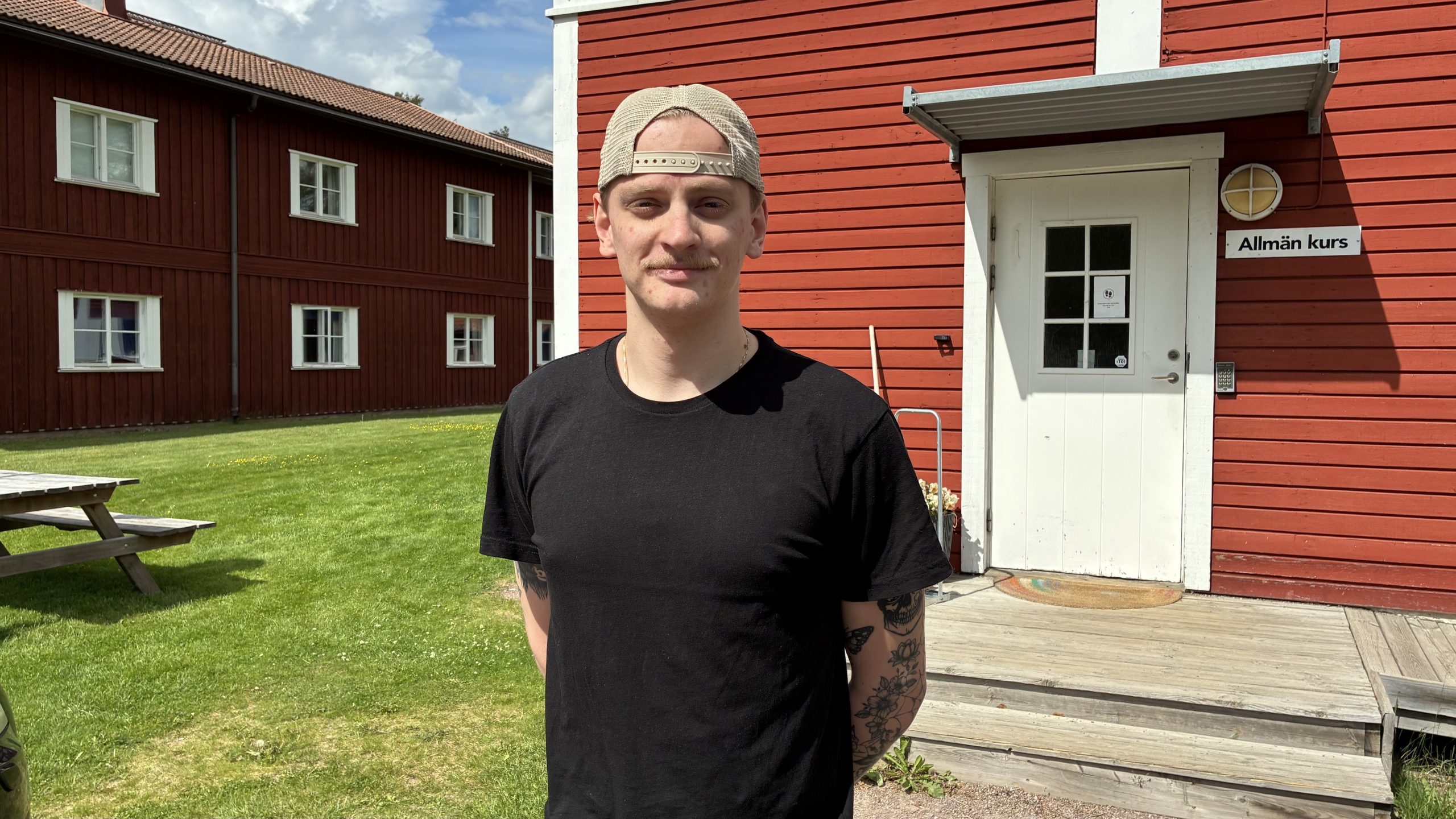 Ung man i bakvänd keps och svart t-shirt på Leksands Folkhögskolas innergård.