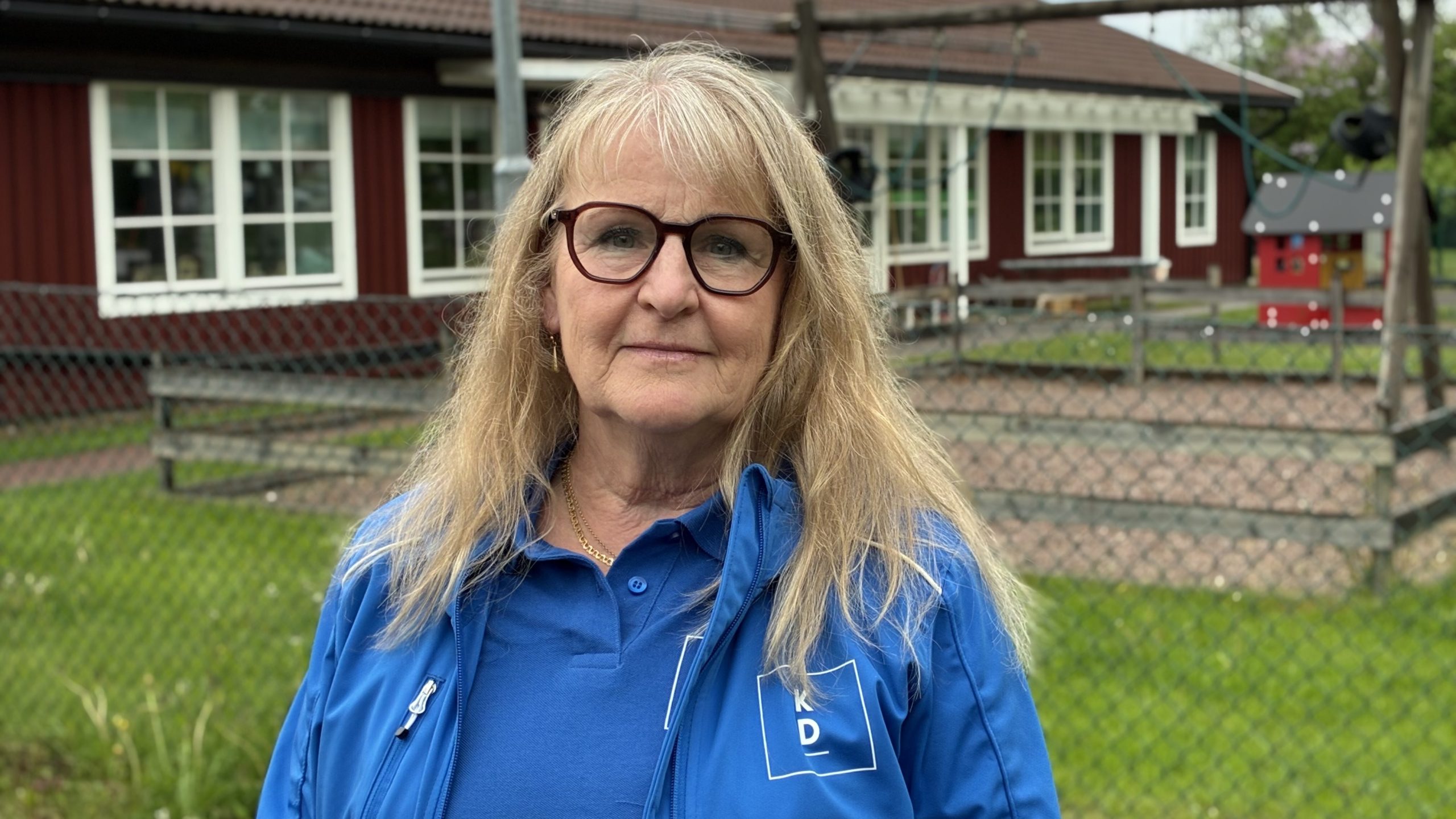 Närbild på Carin Malm med en skolgårdslekplats i bakgrunden.