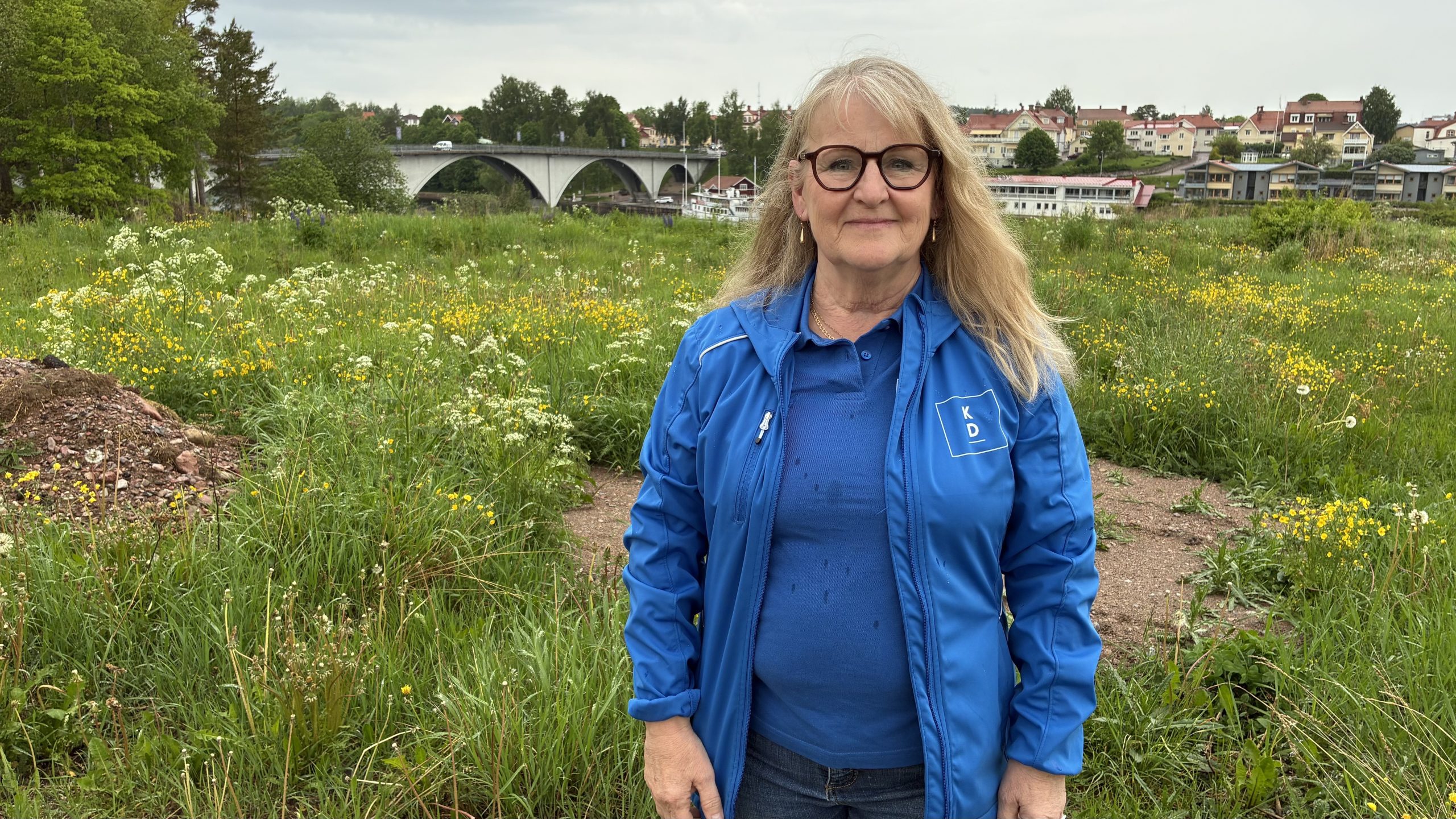Carin Malm fotograferad i partiets blå profilkläder med utsikt mot älven och Leksandsbron i bakgrunden.