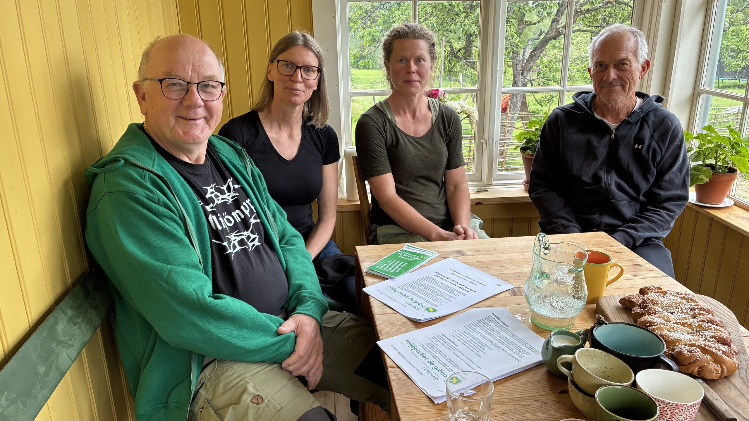 Fyra personer sitter i ett inglasat uterum med Miljöpartiets valprogram på bordet.