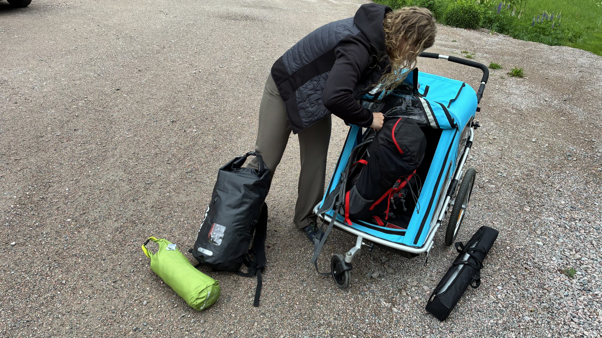 Kvinna står och packar i vattentäta väskor i en löparbarnvagn.