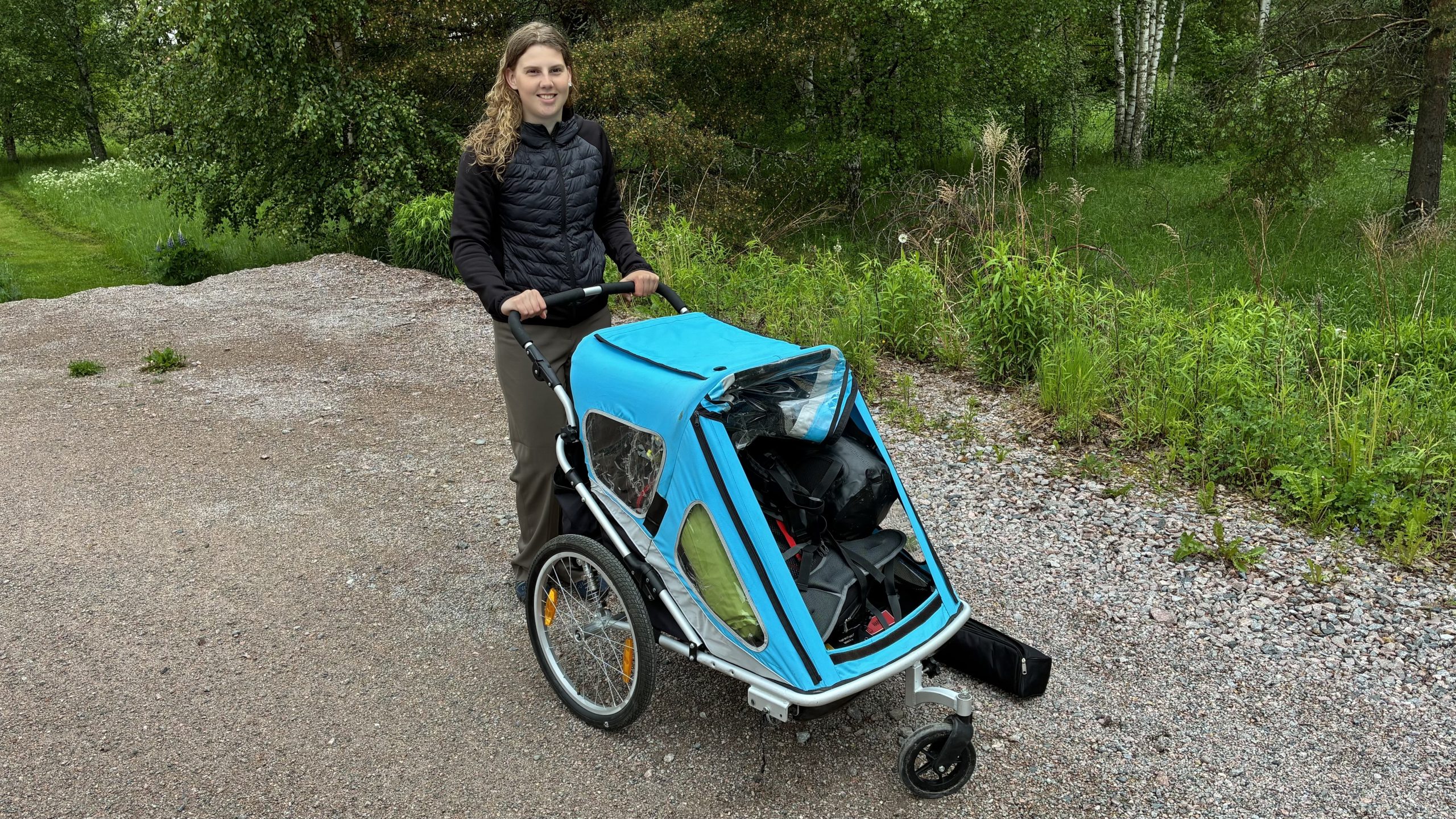 Leende kvinna står bakom en fullpackad löparbarnvagn.