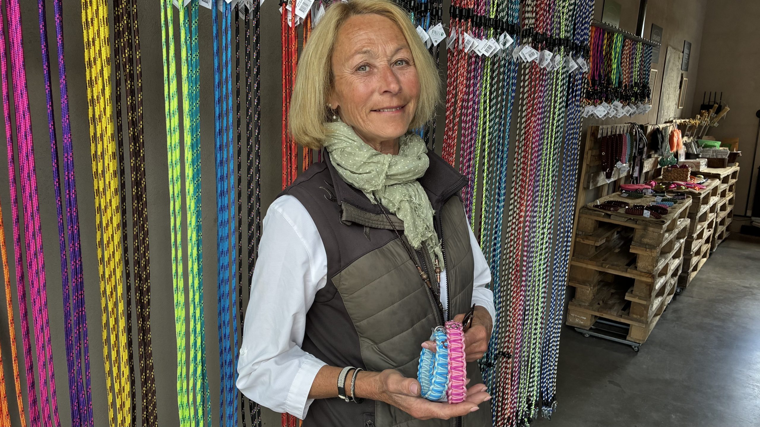 Petronella står framför en rad med linor i olika färger, och håller i små färgglada och fint mönstrade halsband.