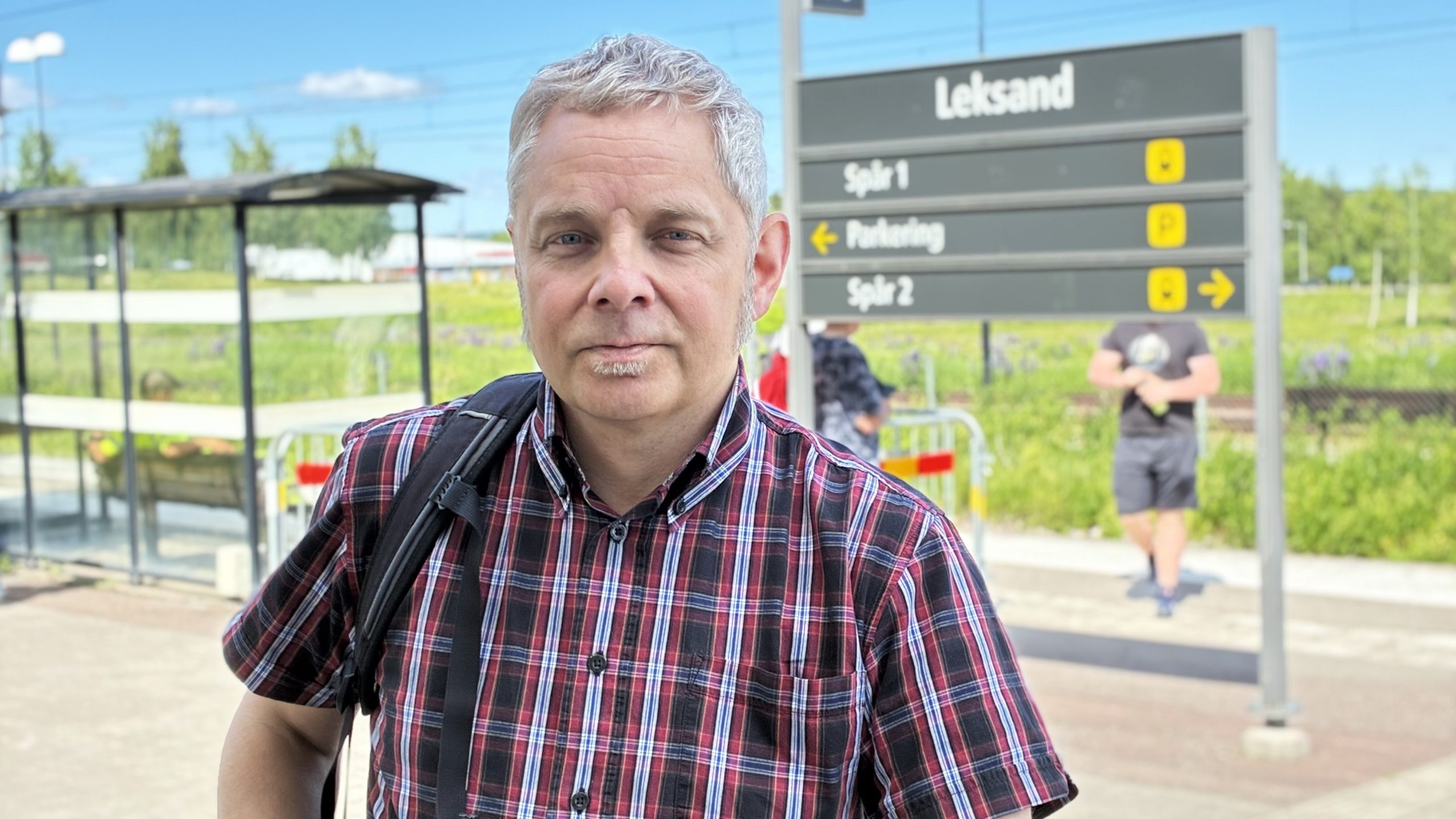 Markus Kummu på en solig dag med Leksands centralstations informationstavla i bakgrunden.