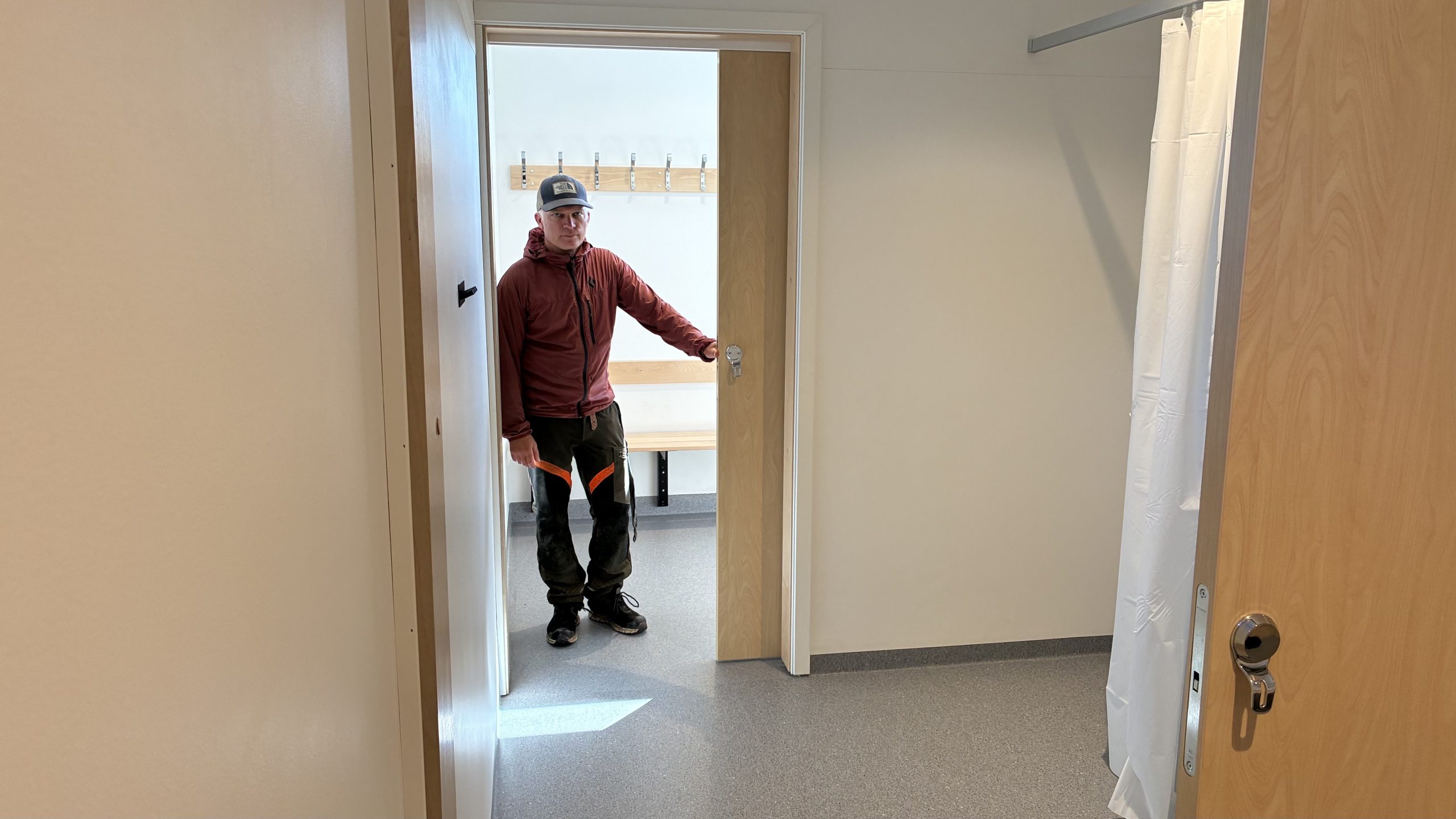 Man i röda arbetskläder håller handen mot en skjutdörr, med några duschbås som syns i förgrunden.