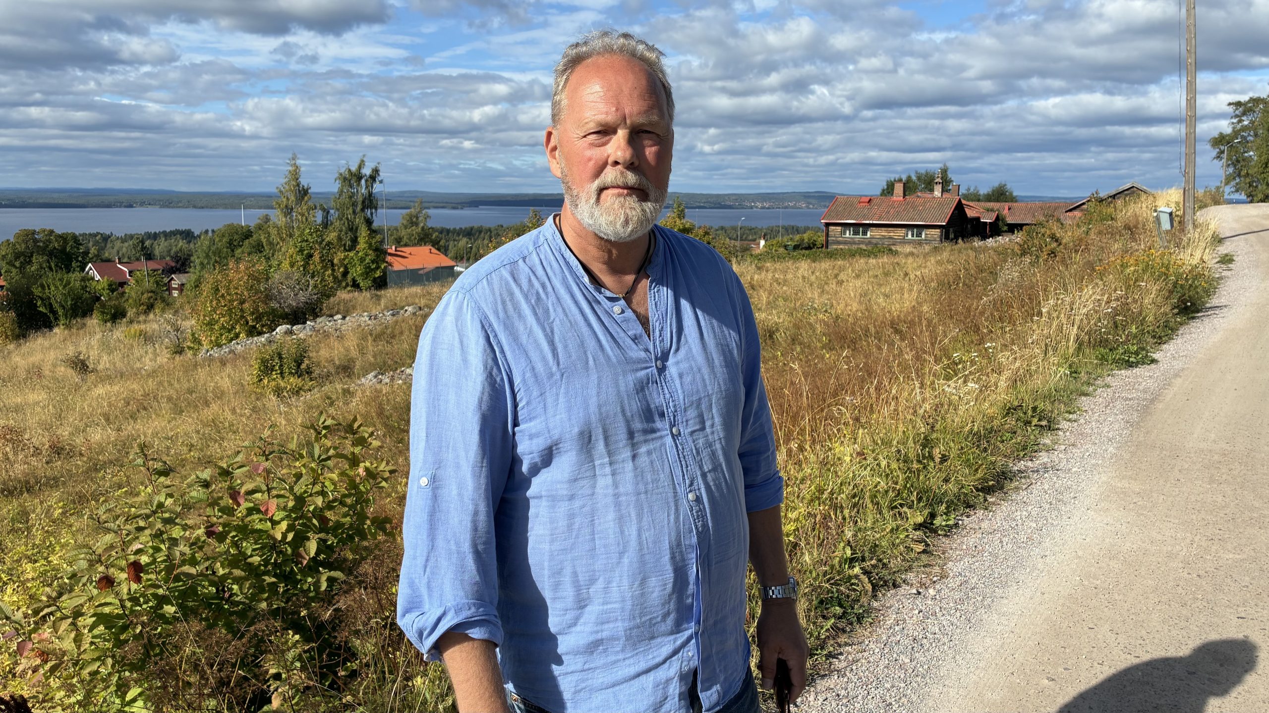 Man i skägg och blå tröja framför en vacker utsikt nedför en sluttning mot Siljan.