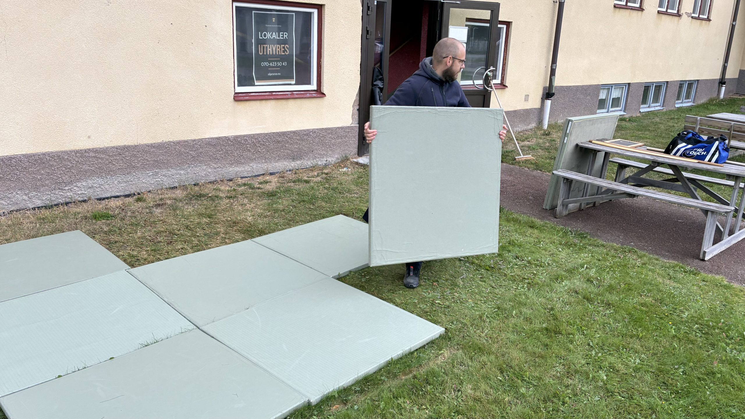 Mats Ahlin bär på gröna vadderade mattor som läggs ut på en innergård i Siljansnäs.
