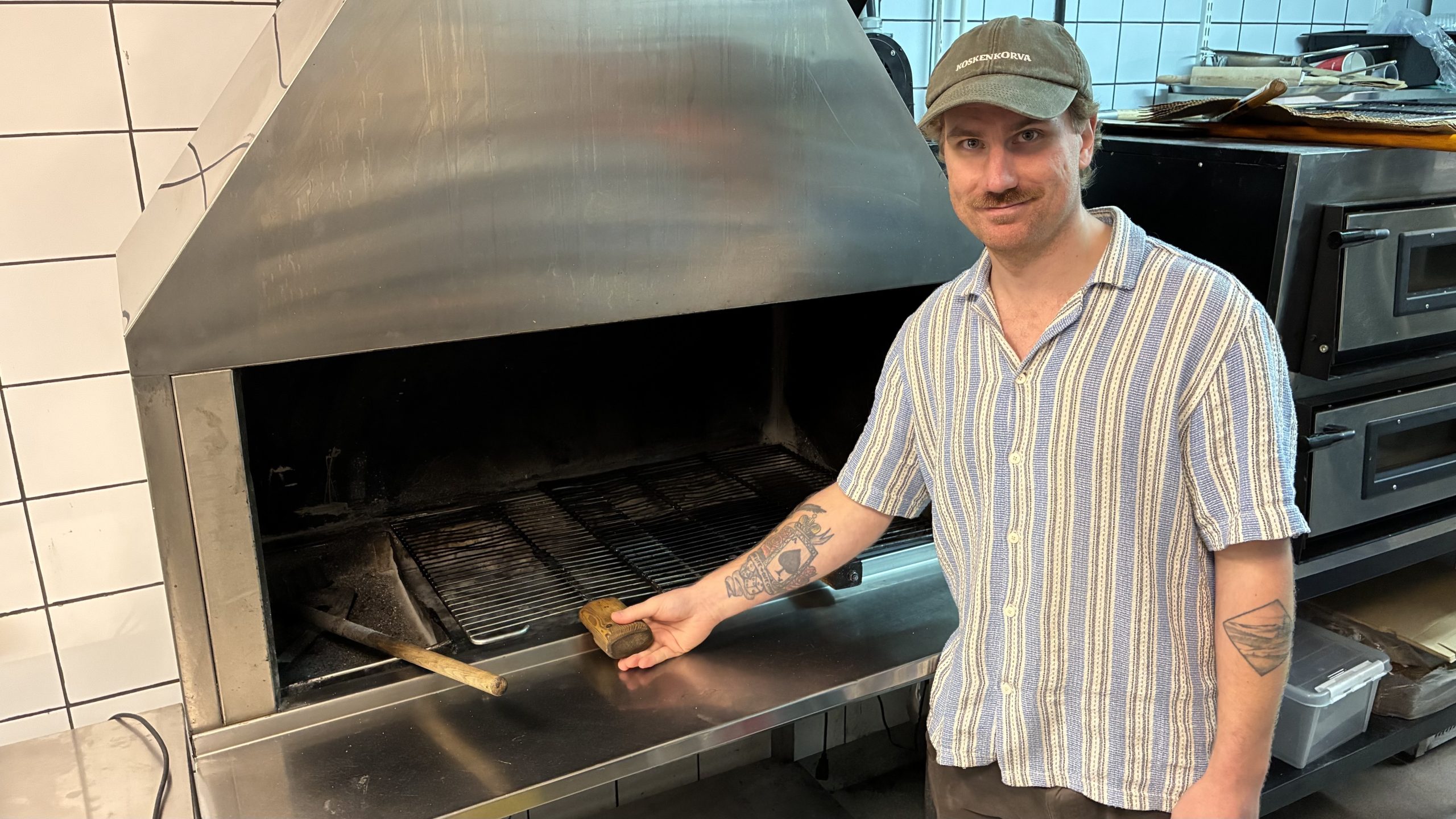 Man med ledig klädsel står vid en släckt kolgrill.