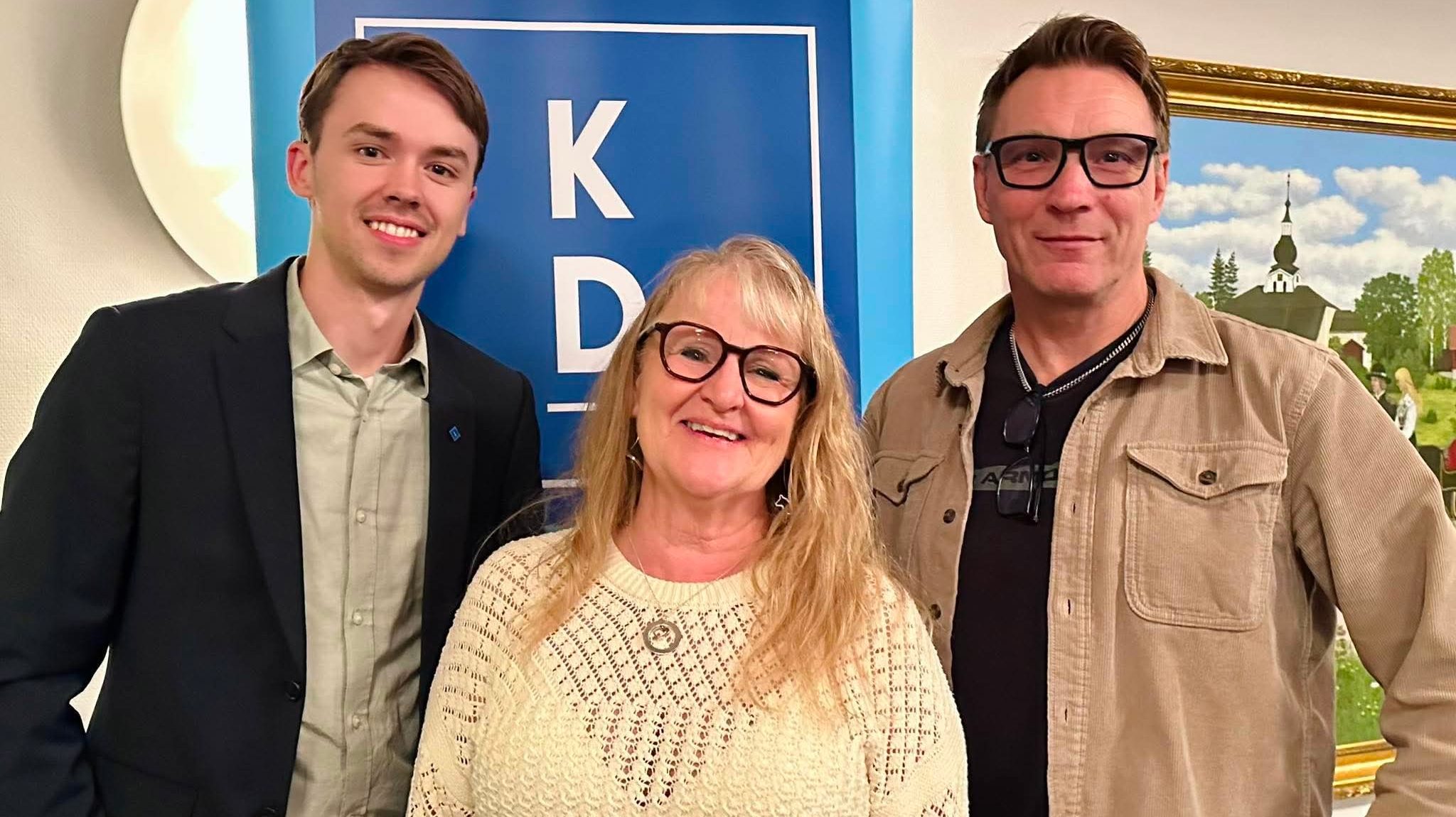 Tre glada personer står uppställda framför en KD-skylt.