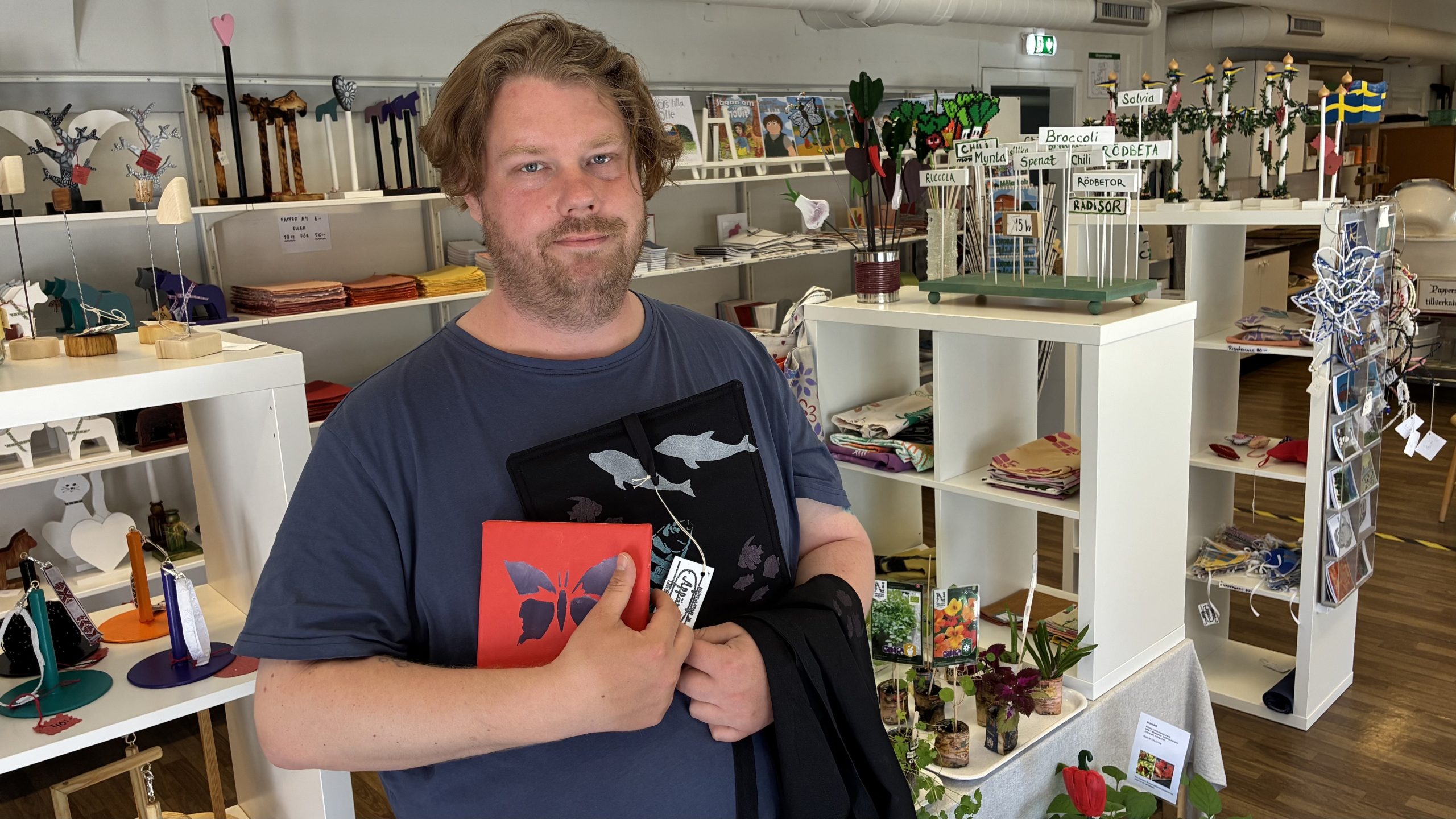 Man står i en butik med inredningsdetaljer och håller i en fin röd disktrasa med ett fjärilsmönster.