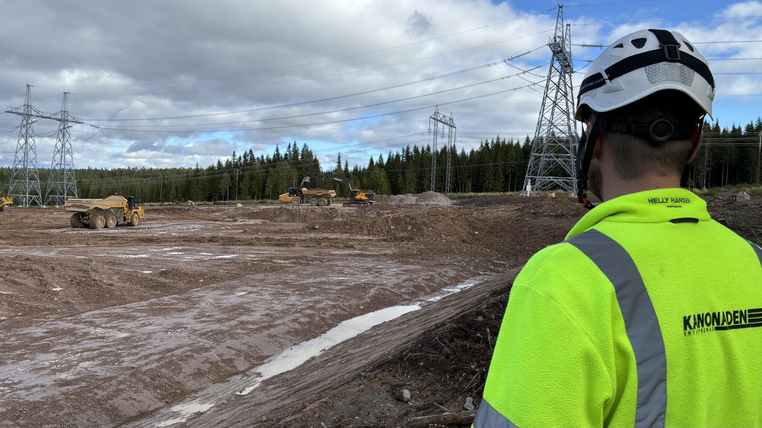 Man i varselkläder och vit hjälm blickar ut över stora ledningsstolpar.