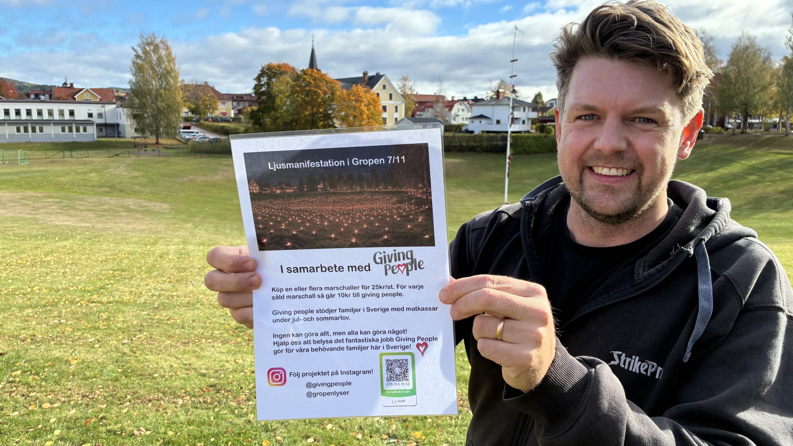 Leende man står vid gropen och håller fram affisch mot kameran.