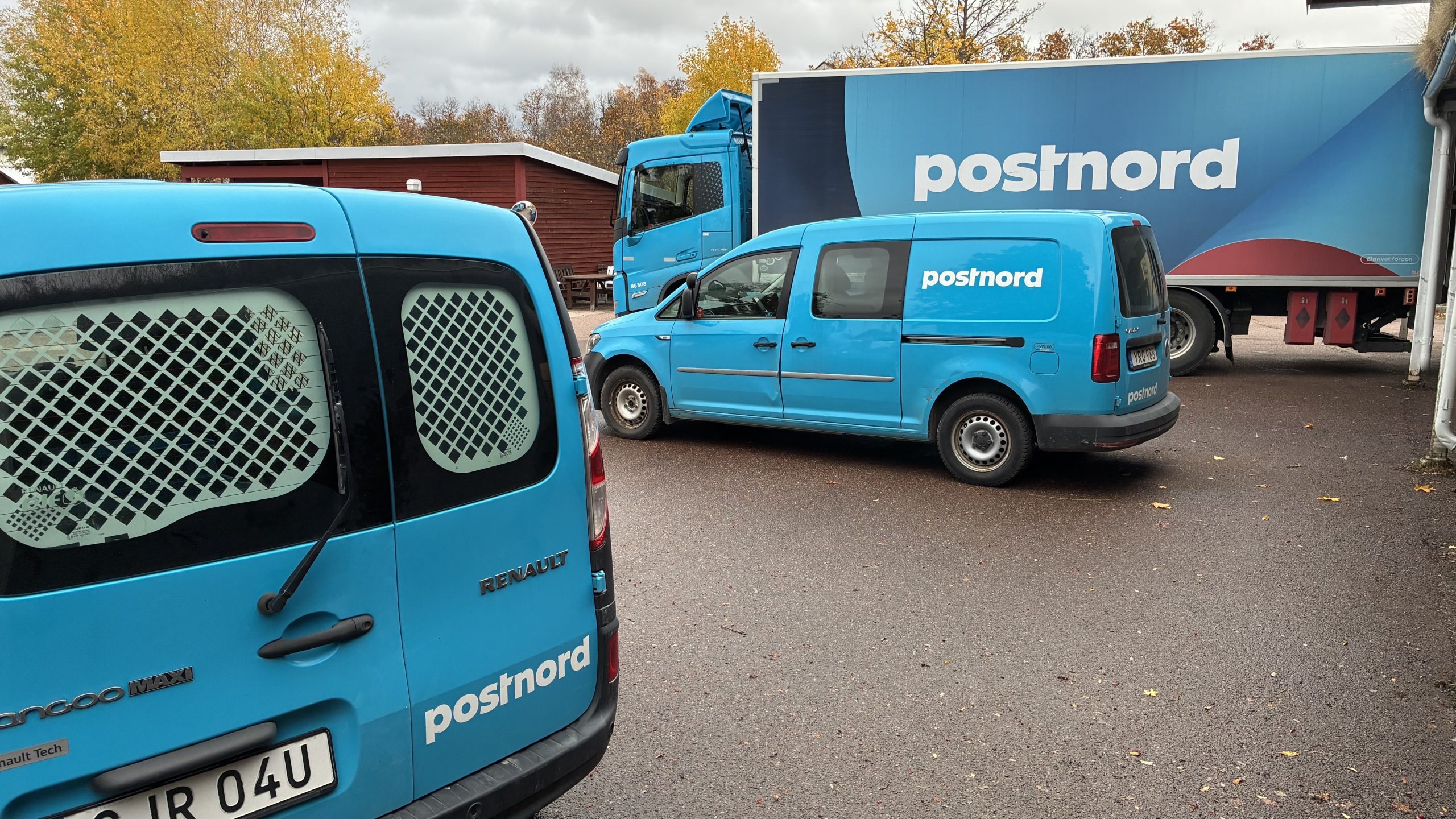 Två blå skåpbilar och en blå lastbil på Postnords parkering i Leksand.
