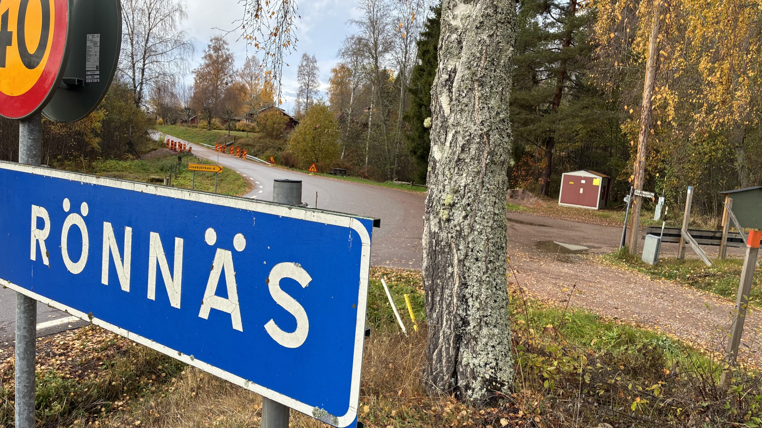Blå vägskylt som visar Rönnäs och 40 km/h i förgrunden, ett vägarbete syns långt bort i bakgrunden.