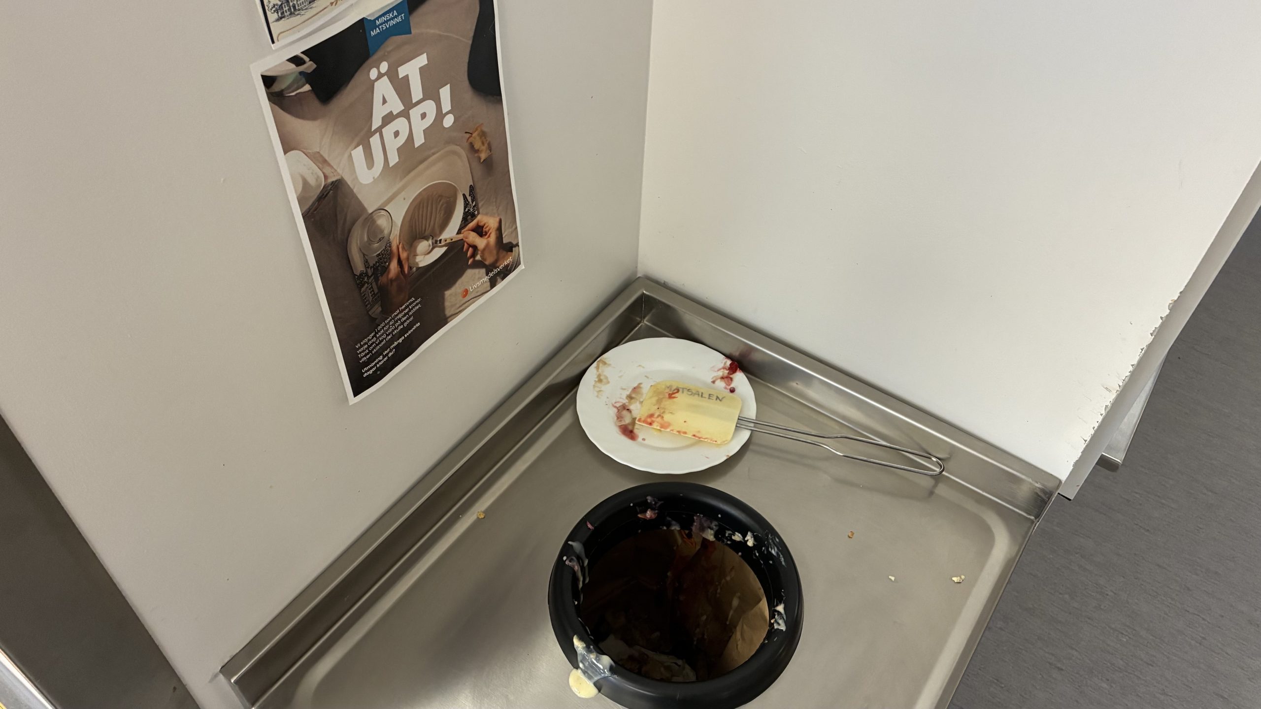 Hål att slänga mat i, med en affisch med texten "Ät Upp!"